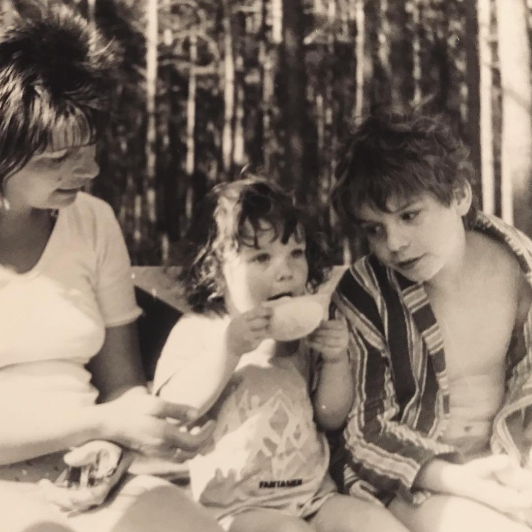 Black and white image of Maria sitting outdoors in between her mother and older brother sitting outdoors eating ice cream.