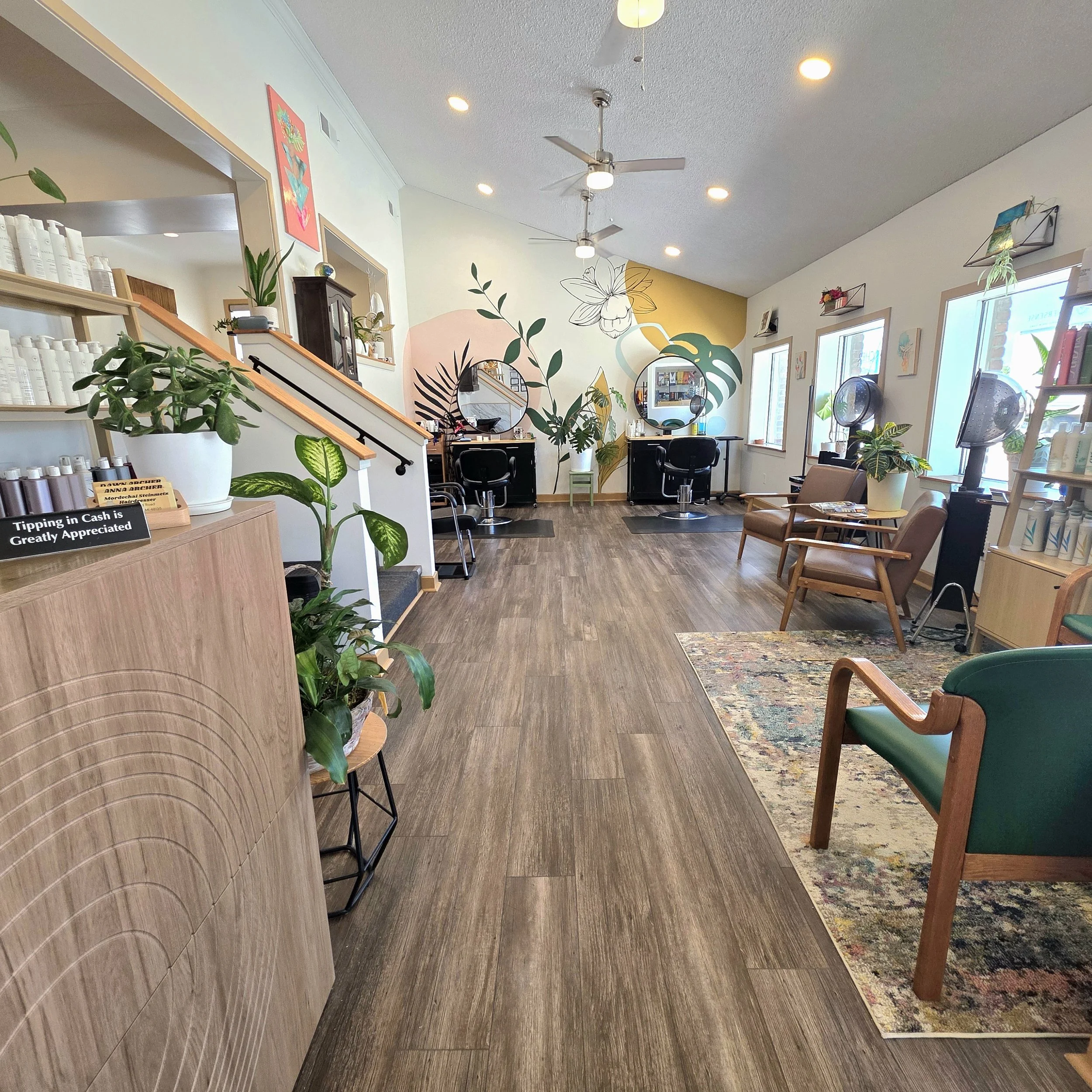 2 archer Salon Garden City Michigan Interior of a hair salon or beauty studio with plants, chairs, mirrors, and art on the walls, ceiling fans, and natural light from windows.