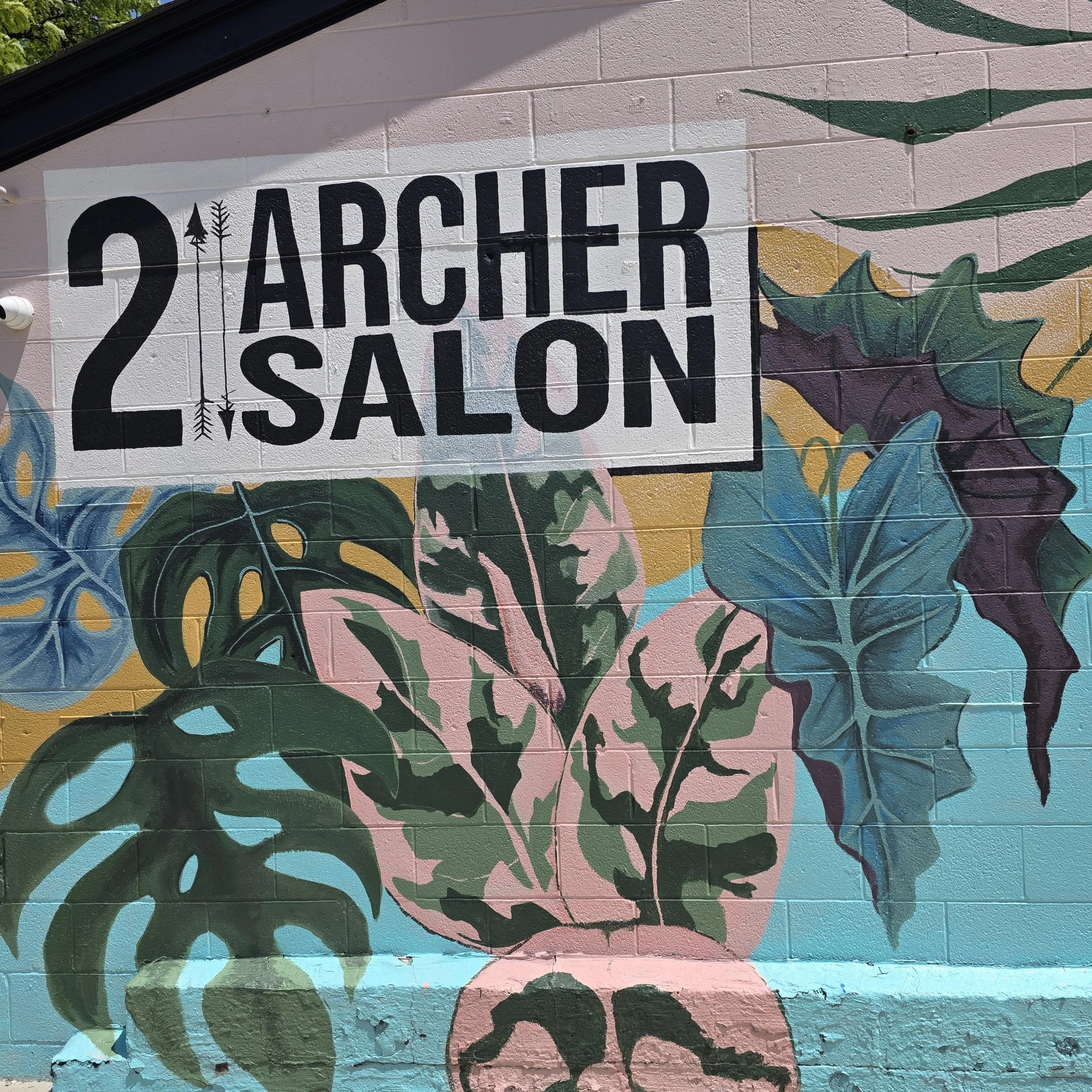 Colorful mural from outside of 2 Archer Salon featuring the text '2 ARCHED 2 SALON' painted on a pink brick wall with decorative floral and leaf designs in green, blue, yellow, and purple.
