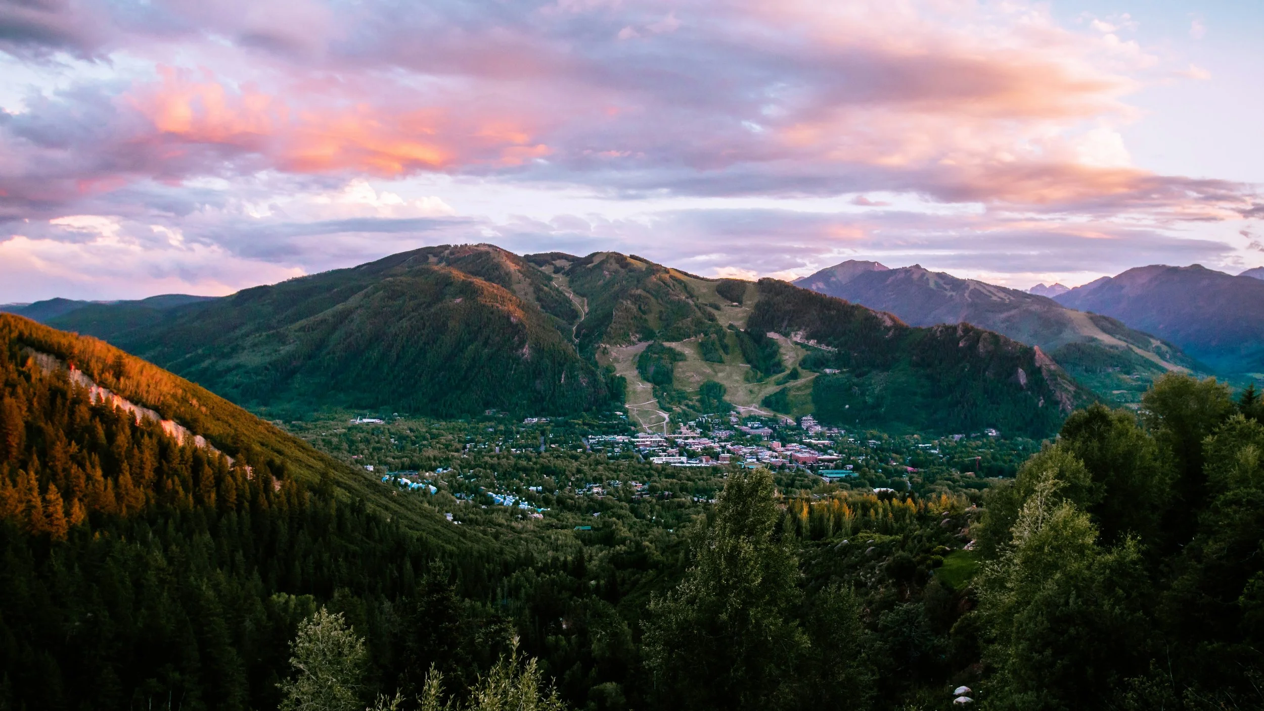 Scenic view of a mountain range during sunset with a small town at the valley floor and a sky filled with colorful clouds.
