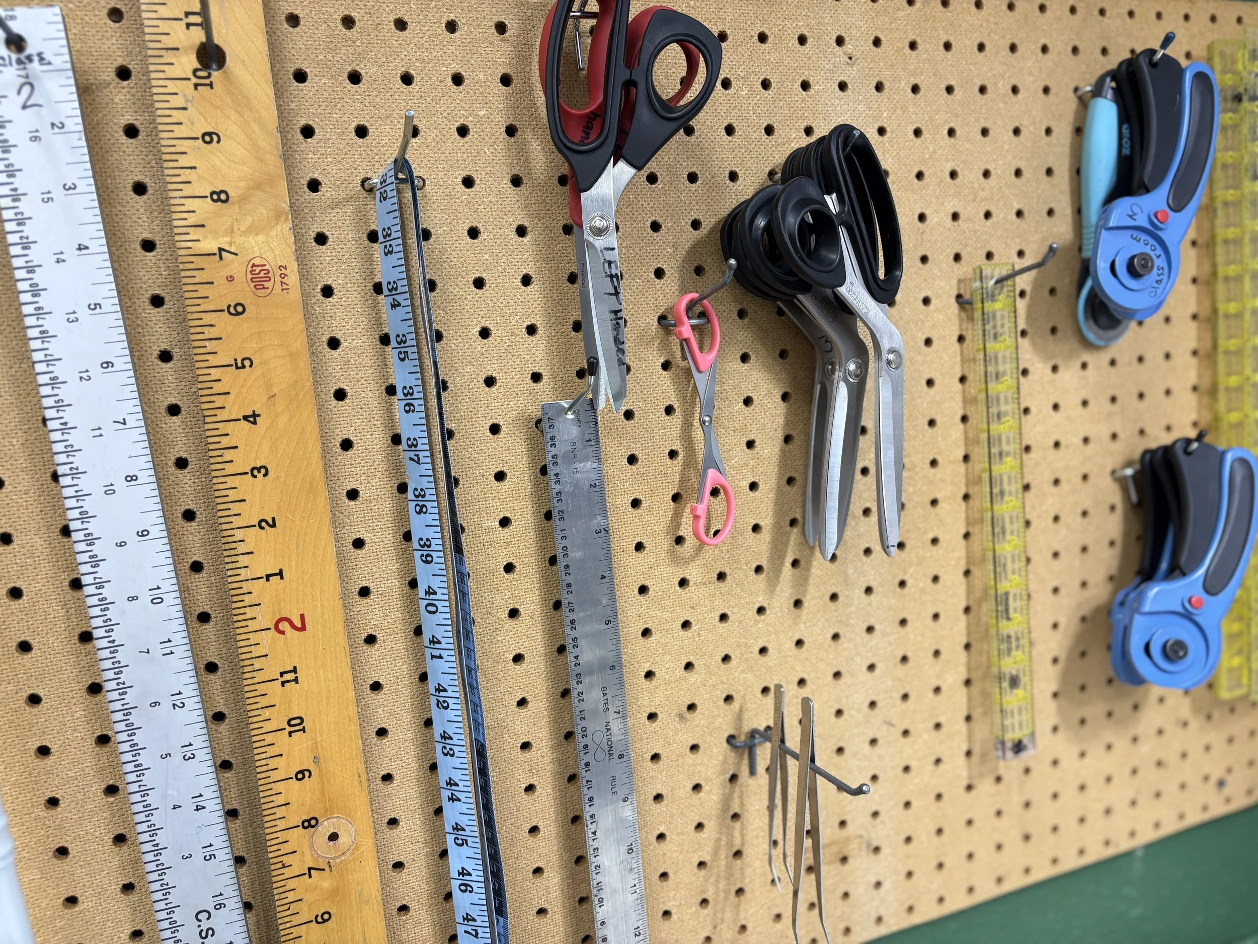 Pearl pegboard with various tools hanging, including scissors, measuring tapes, and wire cutters.