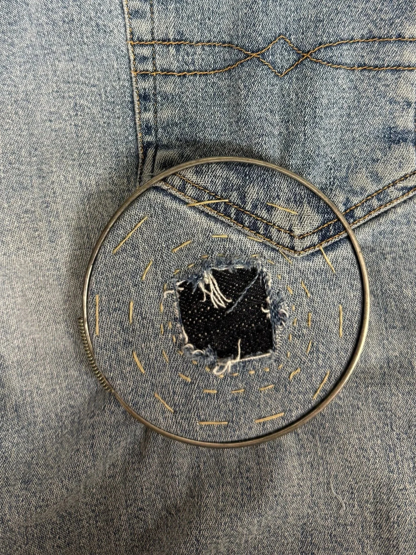 Close-up of a denim repair, mending a hole in jeans using visible reinforcement stitching