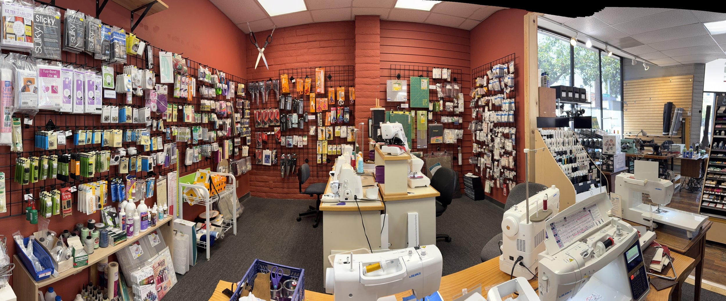 Interior of a specialty craft store with sewing and embroidery supplies, including threads, scissors, and sewing machines, displayed on walls, tables, and shelves.