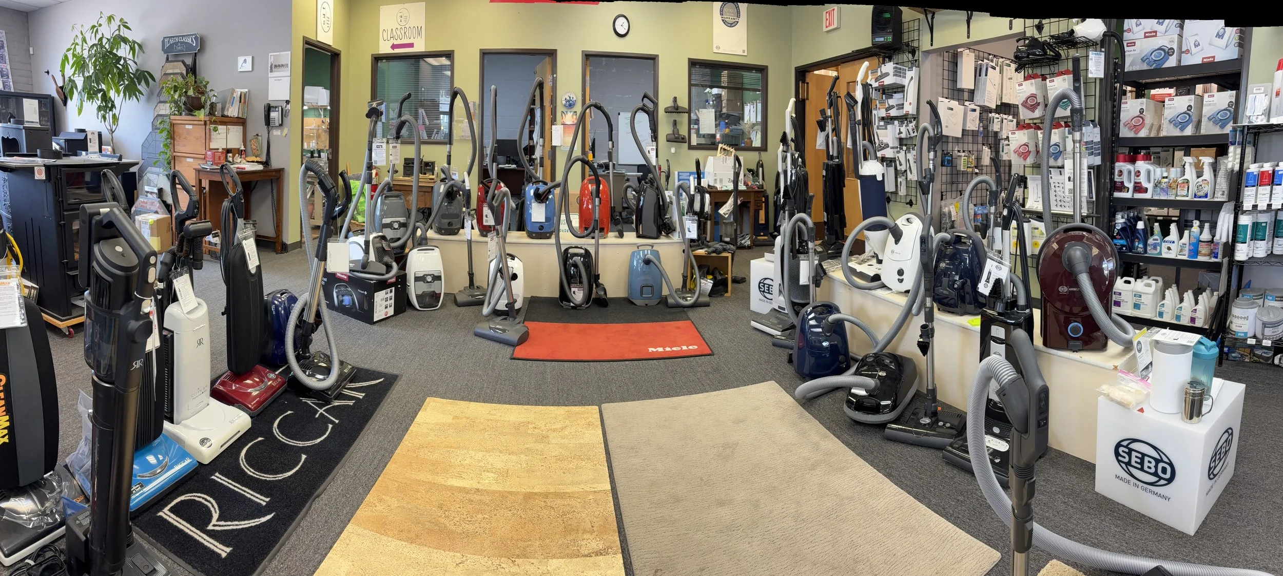 A store with a wide collection of vacuum cleaners and cleaning supplies displayed on shelves and the floor.
