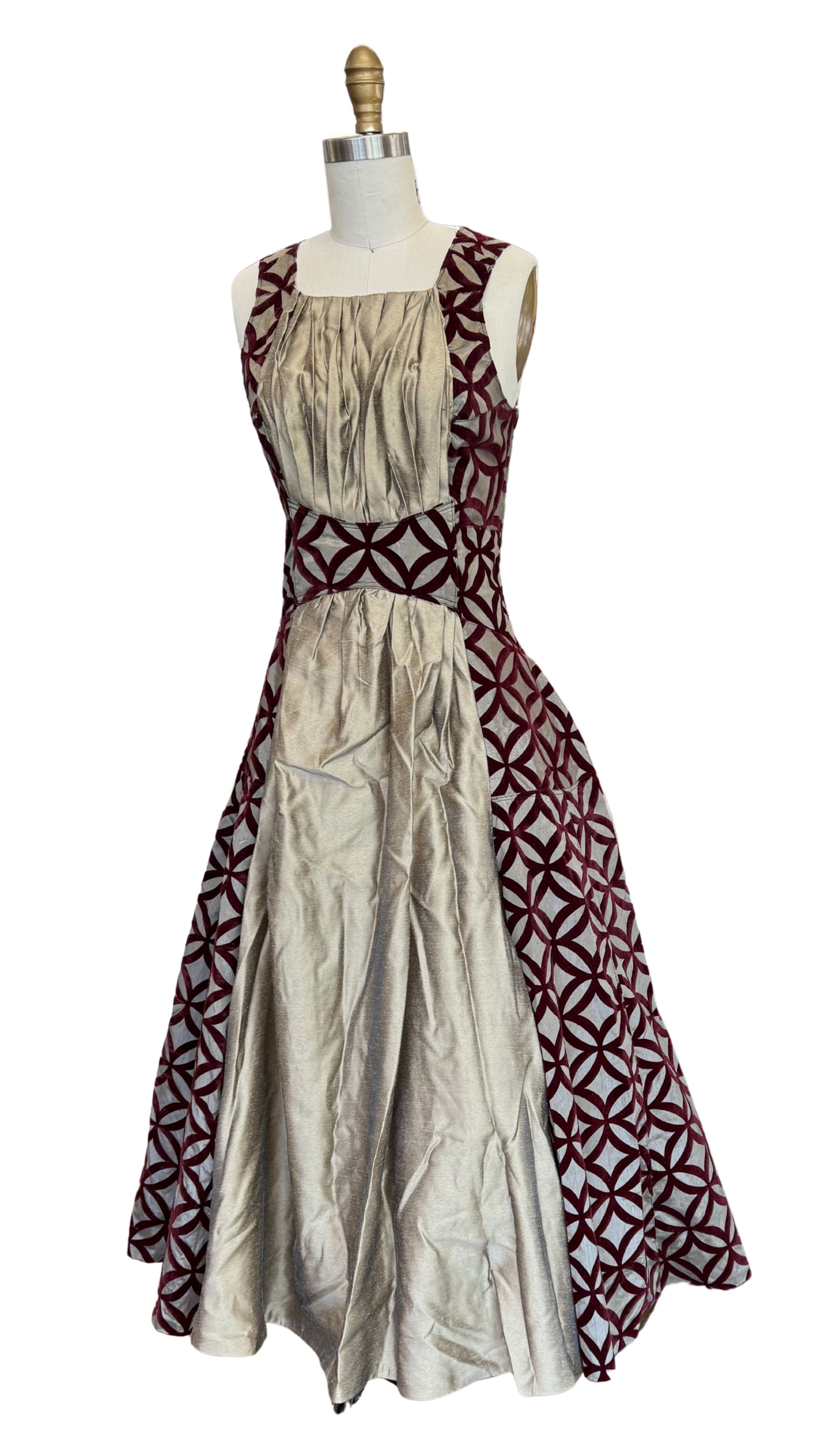 A mannequin wearing a sleeveless long dress with a red geometric pattern and gold satin panels on the front, set against a plain white background.