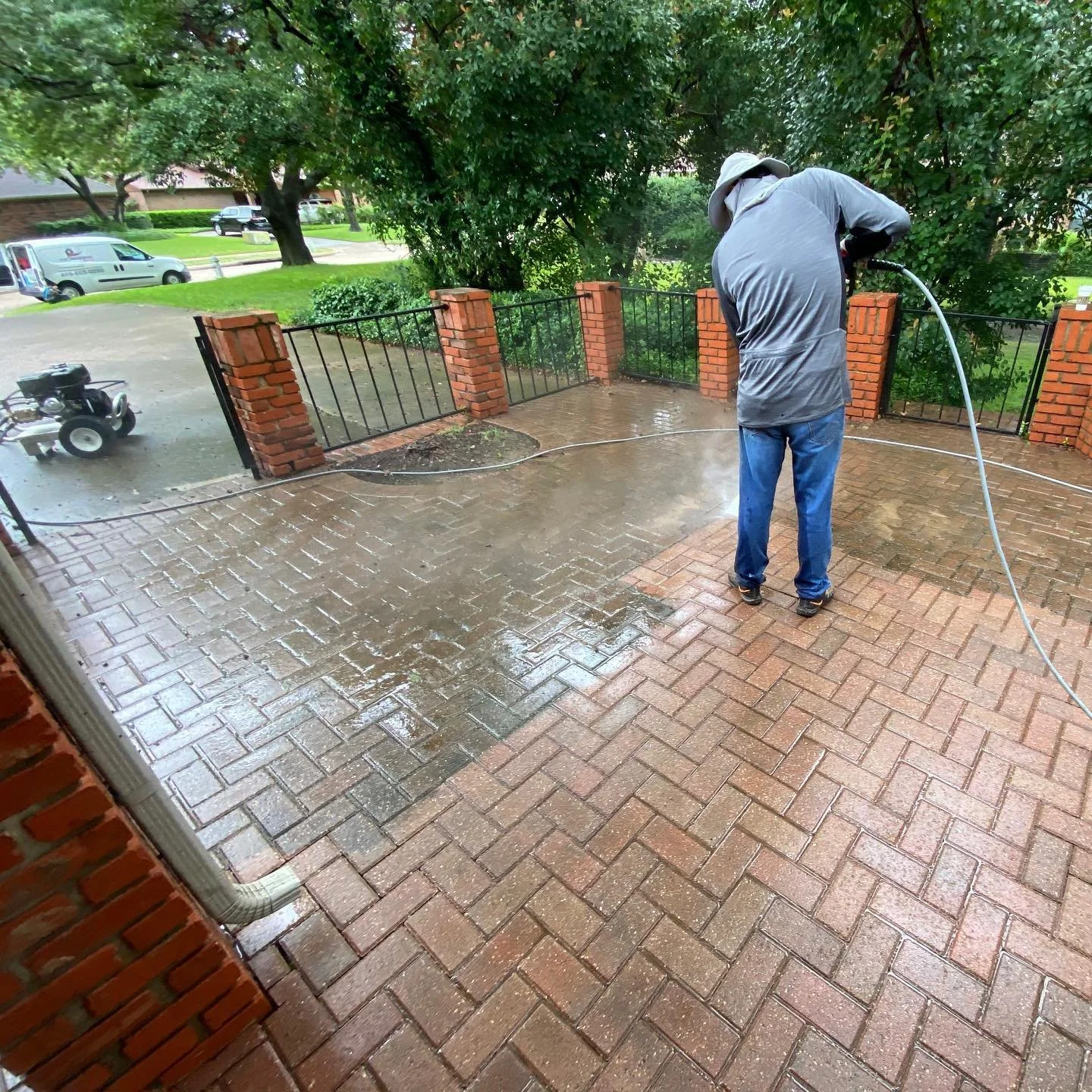 Person pressure washing a brick patio outside a house.