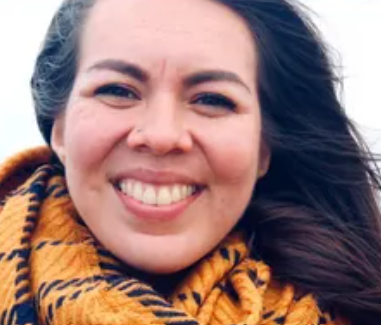 Close-up of a smiling woman with dark hair, wearing a striped scarf, outdoors.