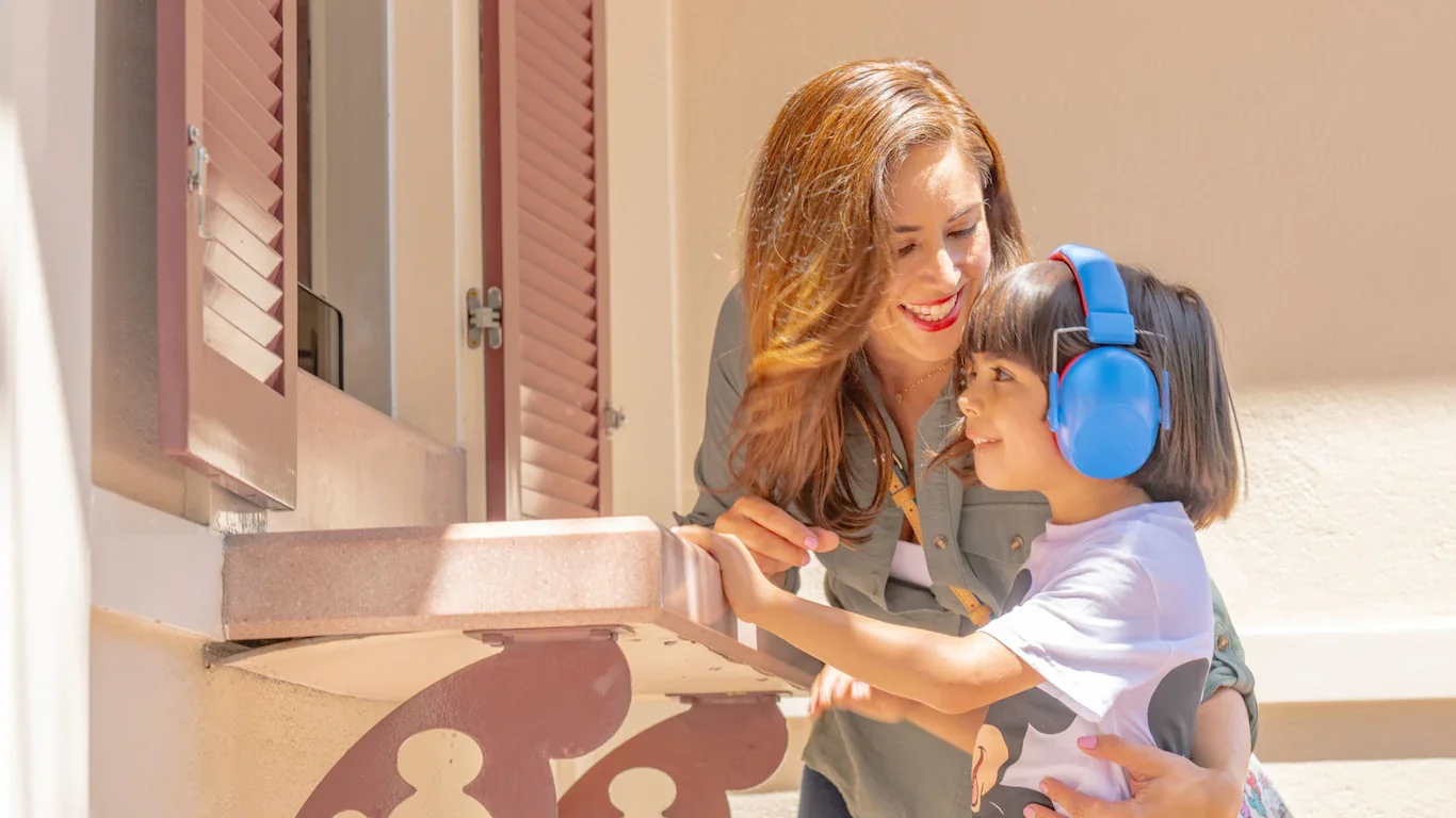 A woman and young girl, possibly a mother and daughter, smiling and enjoying each other's company, with the girl wearing blue headphones.