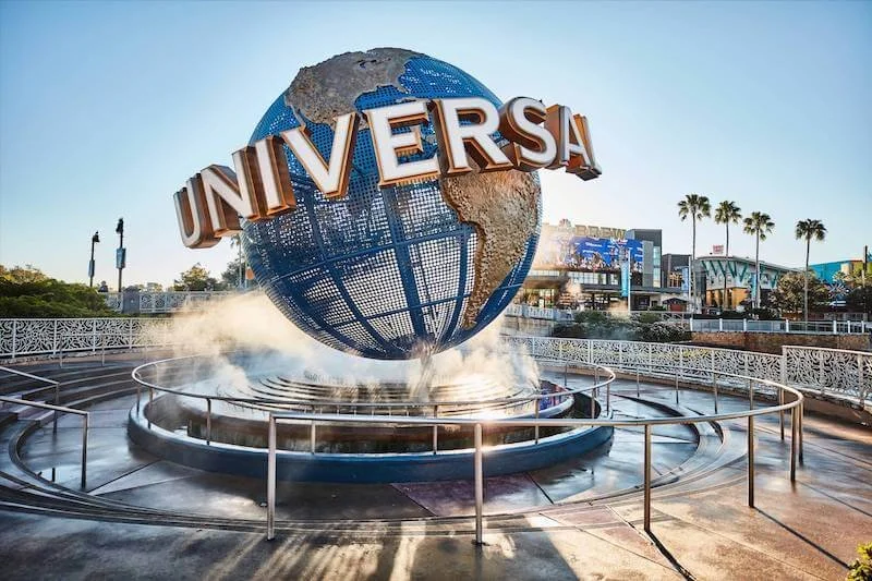 Universal Studios globe fountain with steam, located outdoors with buildings and palm trees in the background.