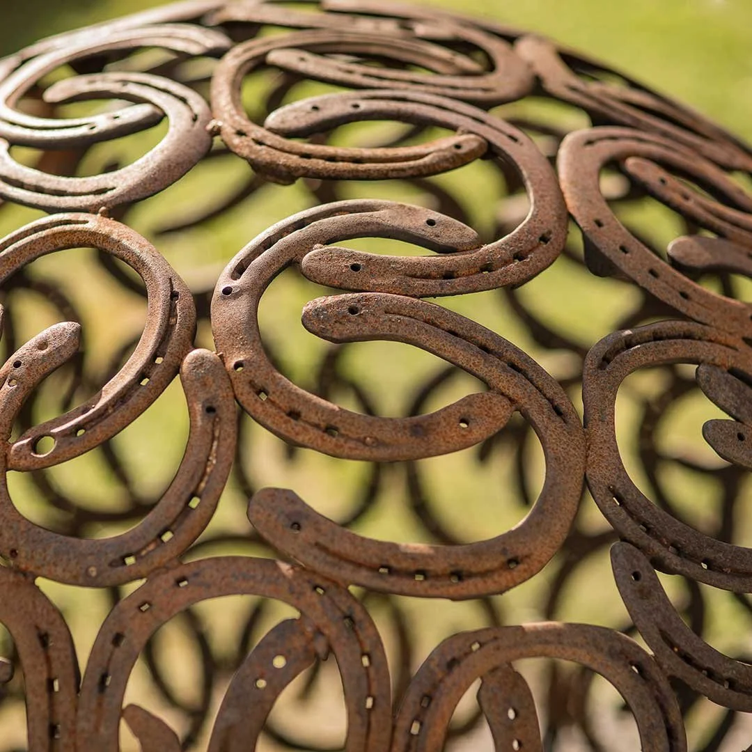 A close-up of many rusty horseshoes piled together on a green grass background.