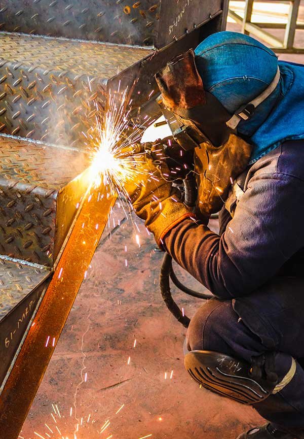 A person welding a metal structure with sparks flying in an industrial workshop.