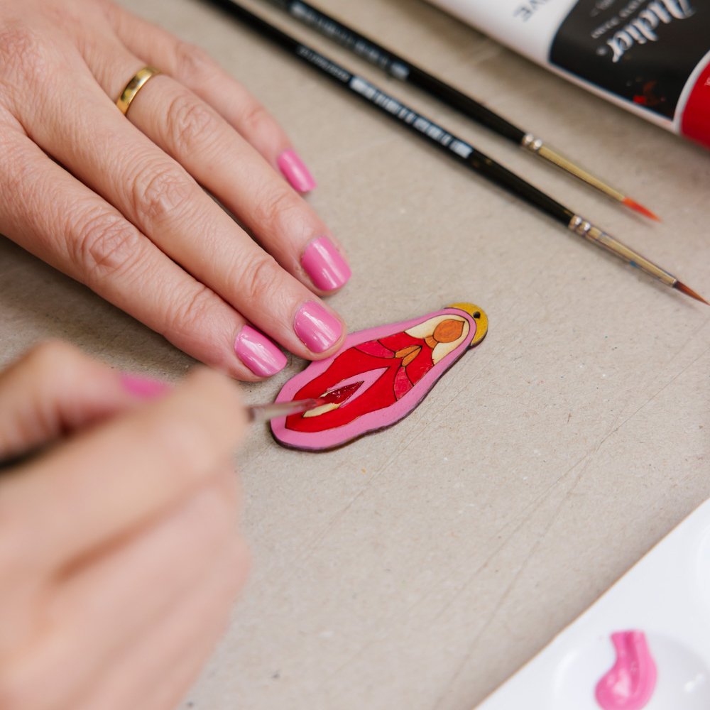 Person painting a cartoon mermaid figure pink and red, with pink nail polish on their nails.