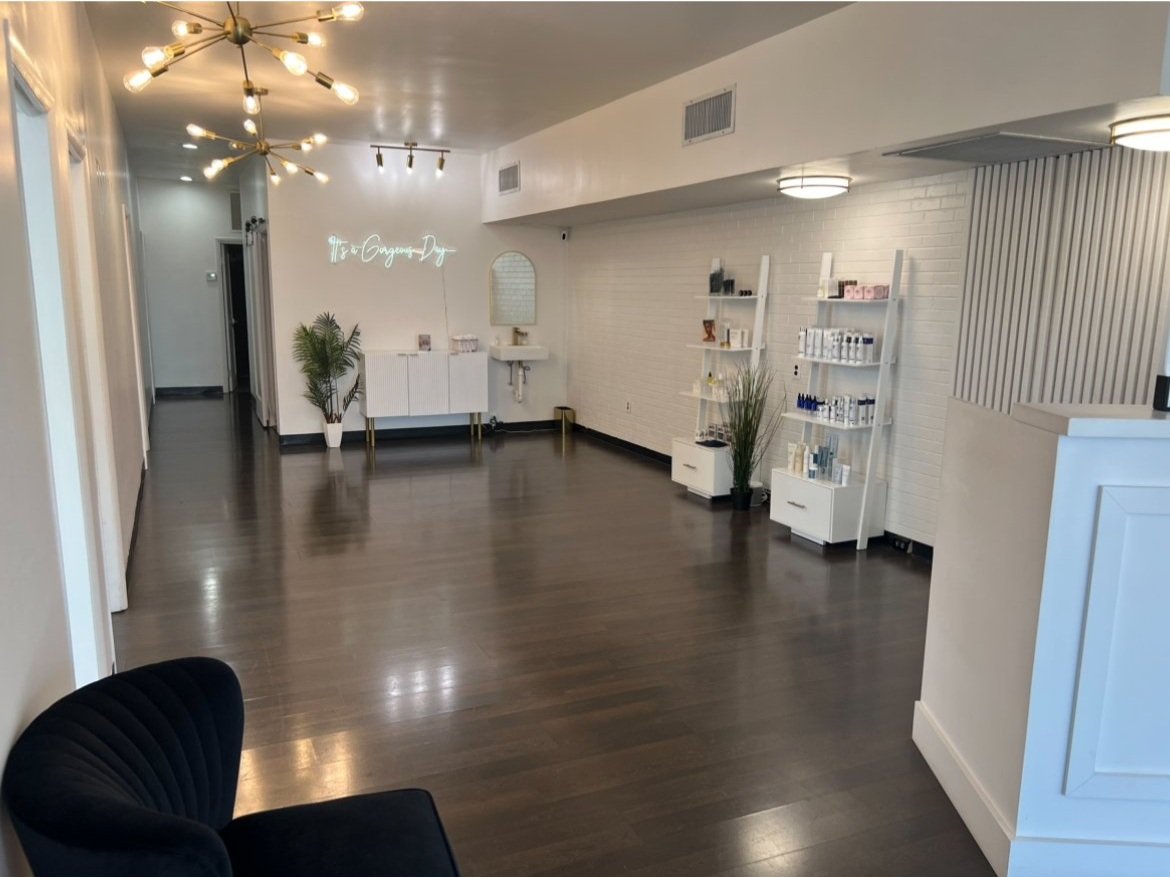 Empty boutique with white walls, dark wood flooring, modern light fixtures, and shelves displaying skincare or beauty products.