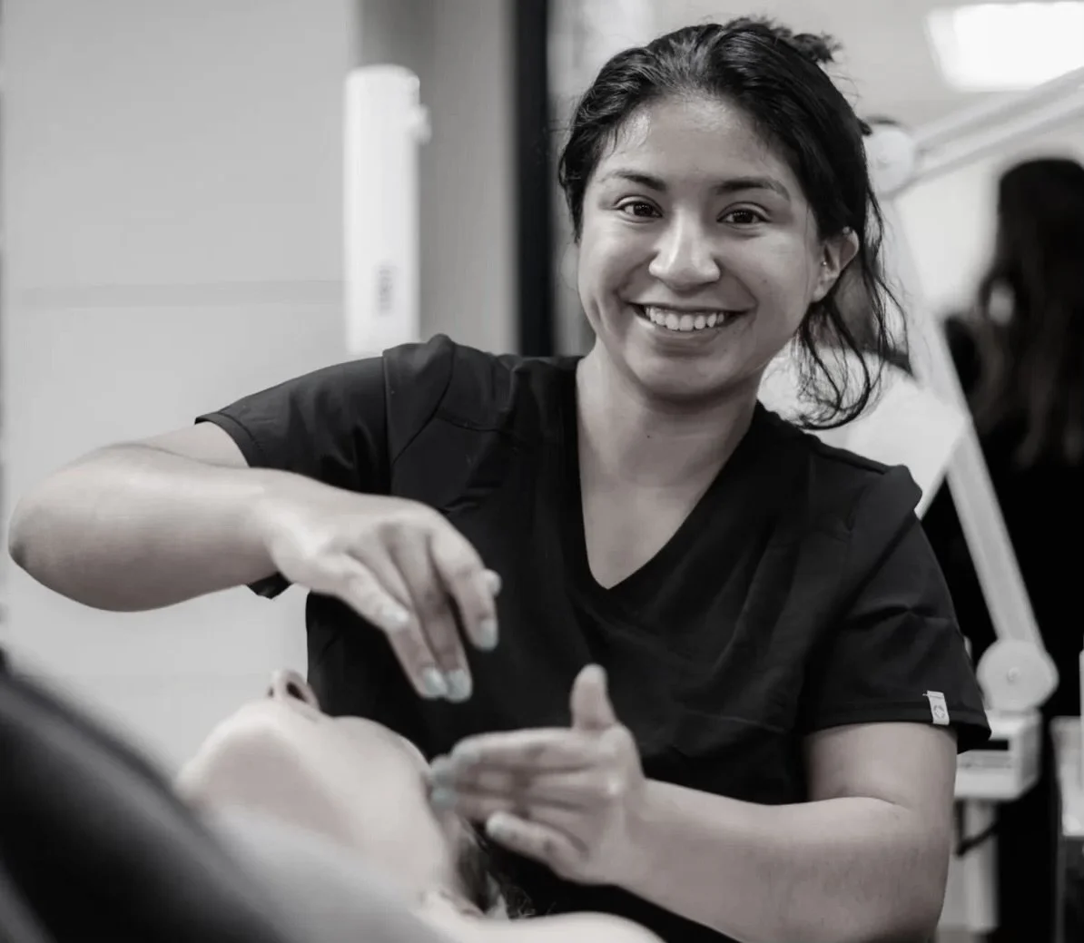 A smiling female healthcare professional in a black uniform treats a patient in a medical setting.