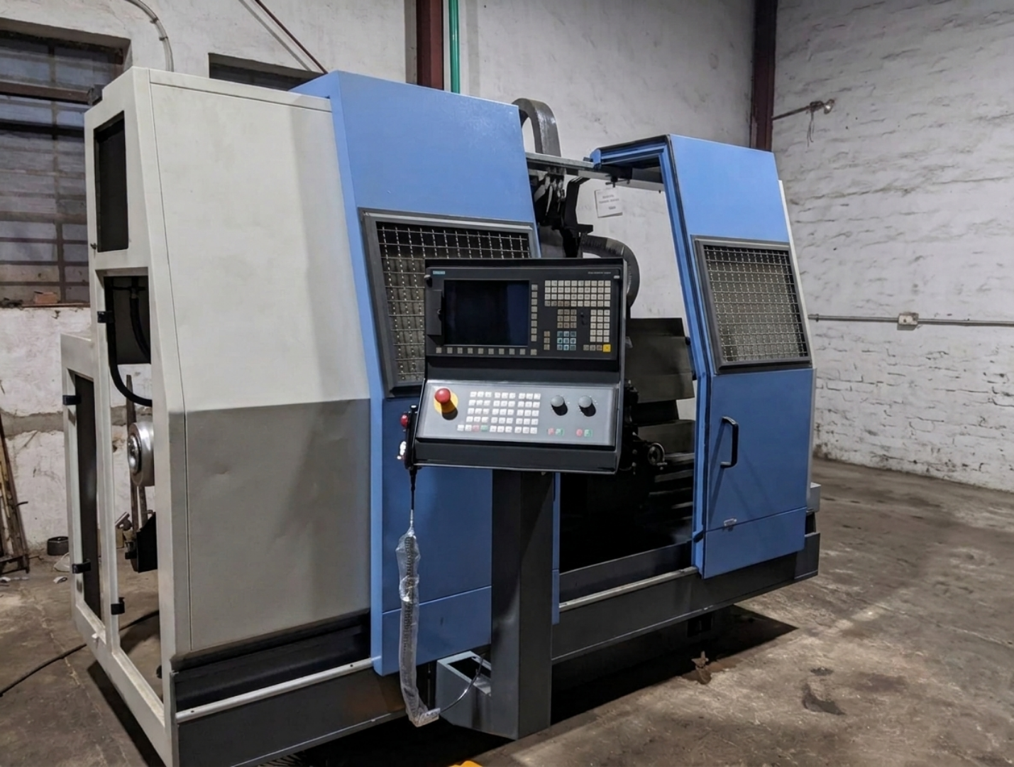 Una máquina CNC industrial en un taller, color azul y gris, con un panel de control con botones y pantalla.