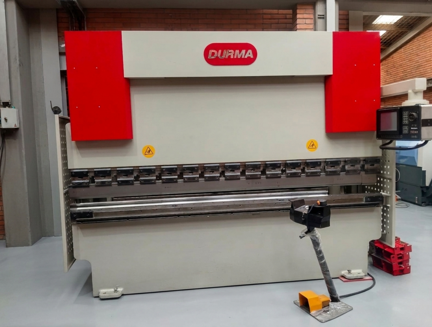 Máquina de corte industrial marca Durma en un entorno de fábrica, con estructura metálica, pantallas de control y señalización de advertencia.