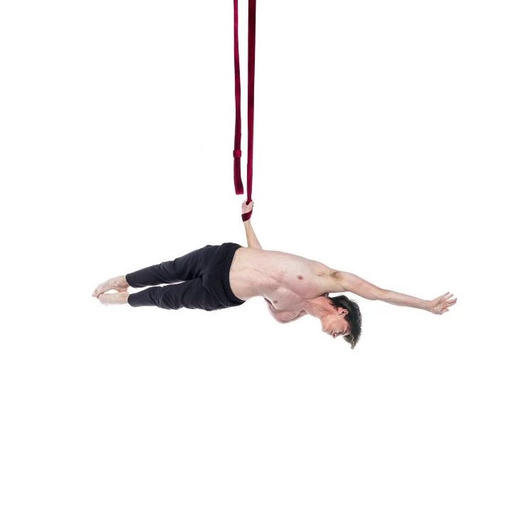 A man hanging upside down from red straps with his body extended horizontally, with a white background.