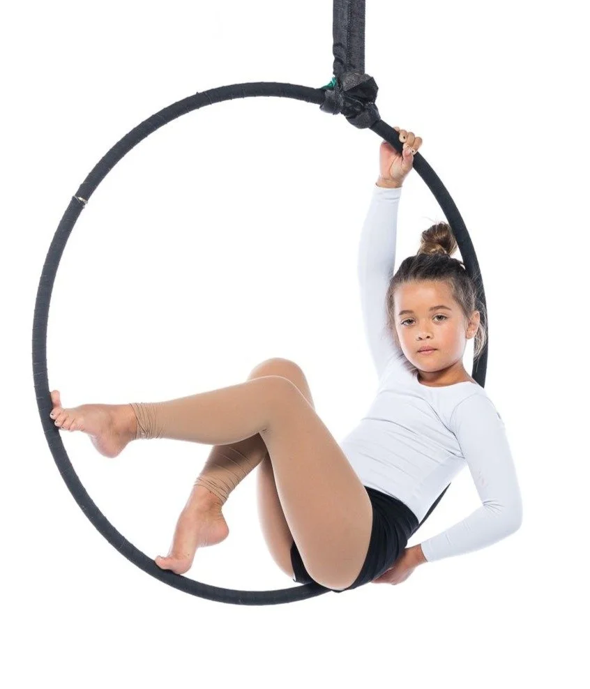 Young girl performing on a circular aerial hoop or lyra, hanging from a black fabric strap with a white background.