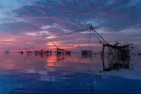 Sunset over a body of water with several abandoned fishing structures and docks reflected on the surface.