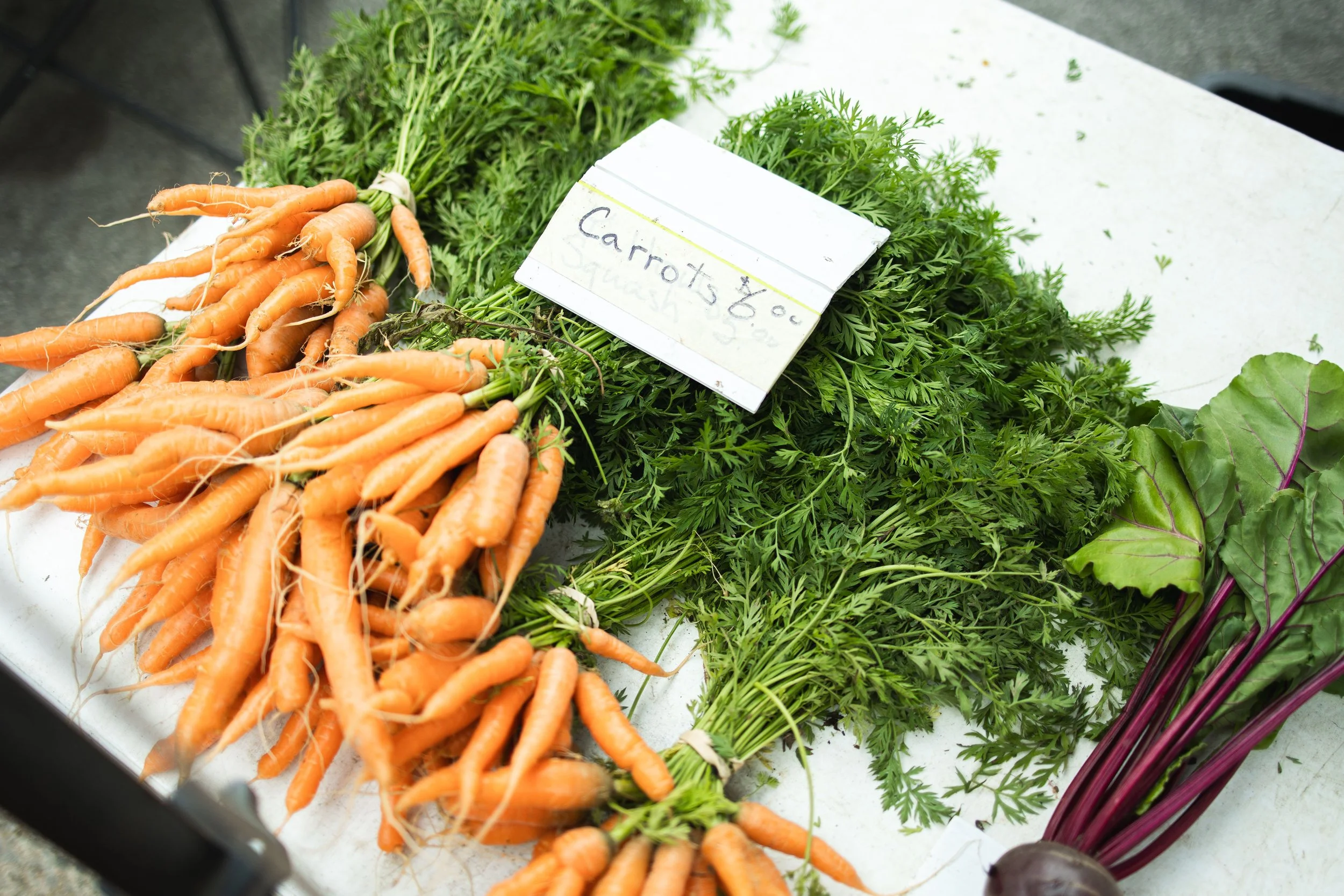 Fresh carrots with green tops, leafy greens, and beets on display at a market