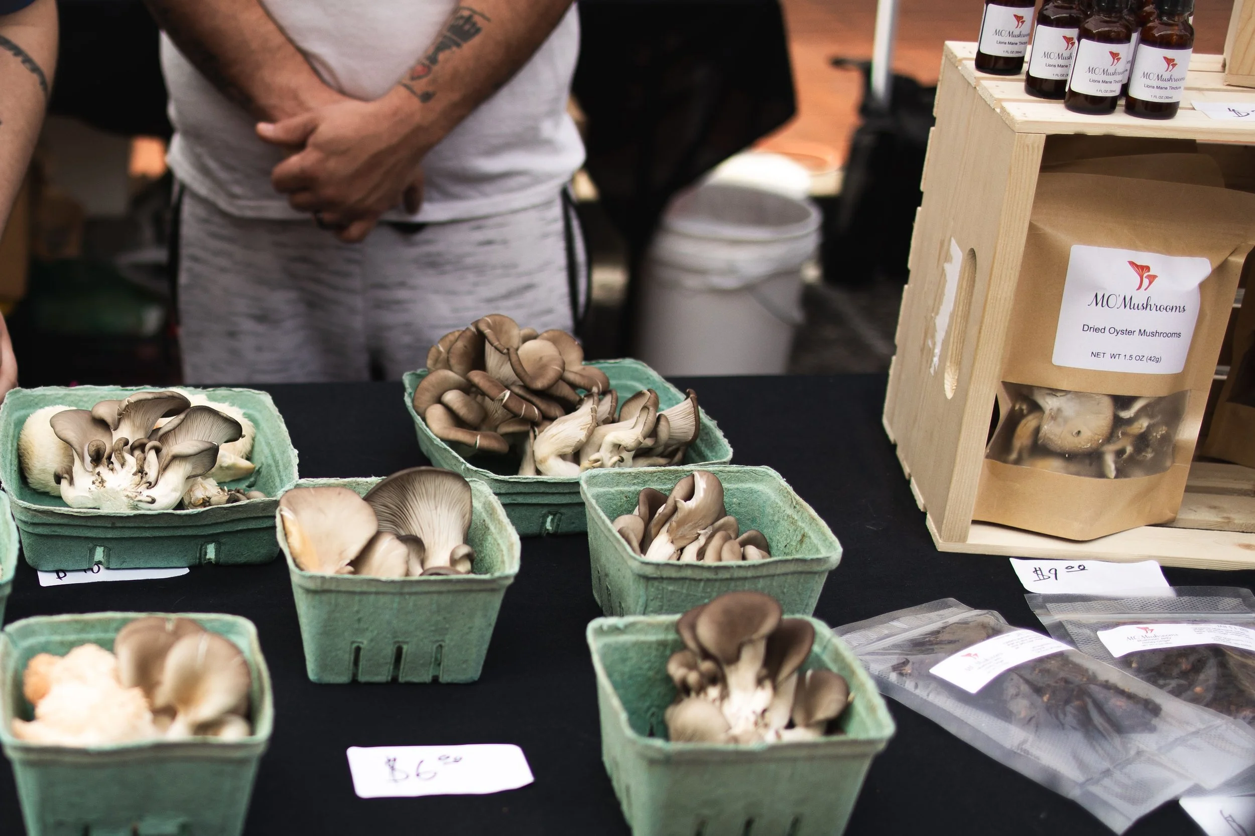 Various mushroom varieties placed in green containers and a wooden box at a market stall.