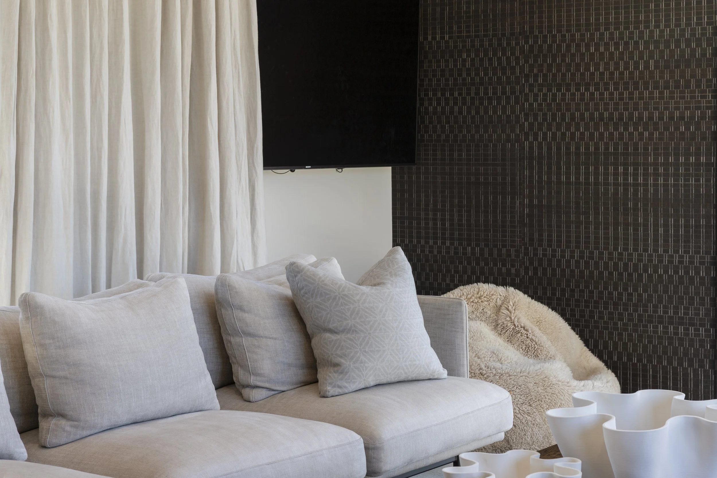 Living room with a white sofa with multiple white pillows, textured throw blanket, black patterned accent wall, and white curtains.