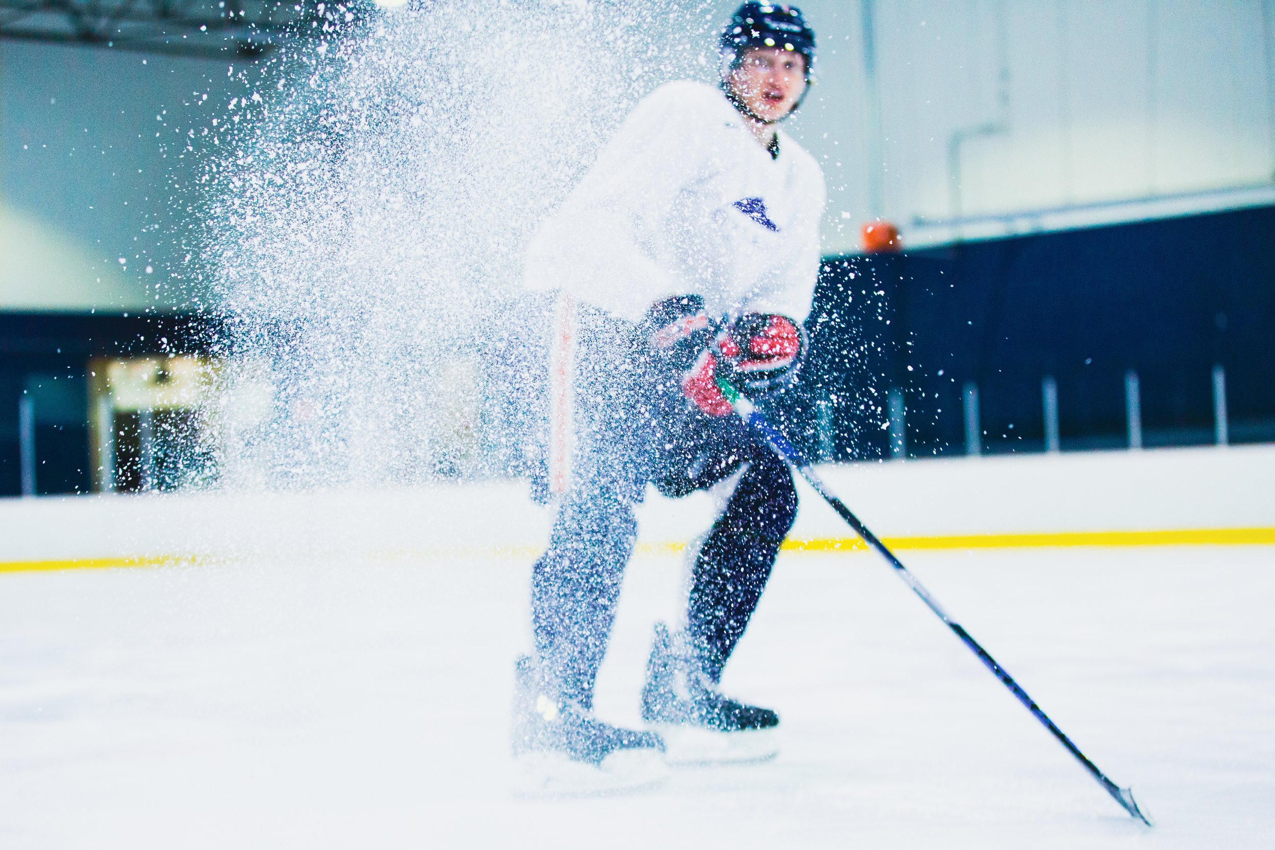 A hockey player in a white jersey and black helmet falling on the ice, with snow flying around him during a game.