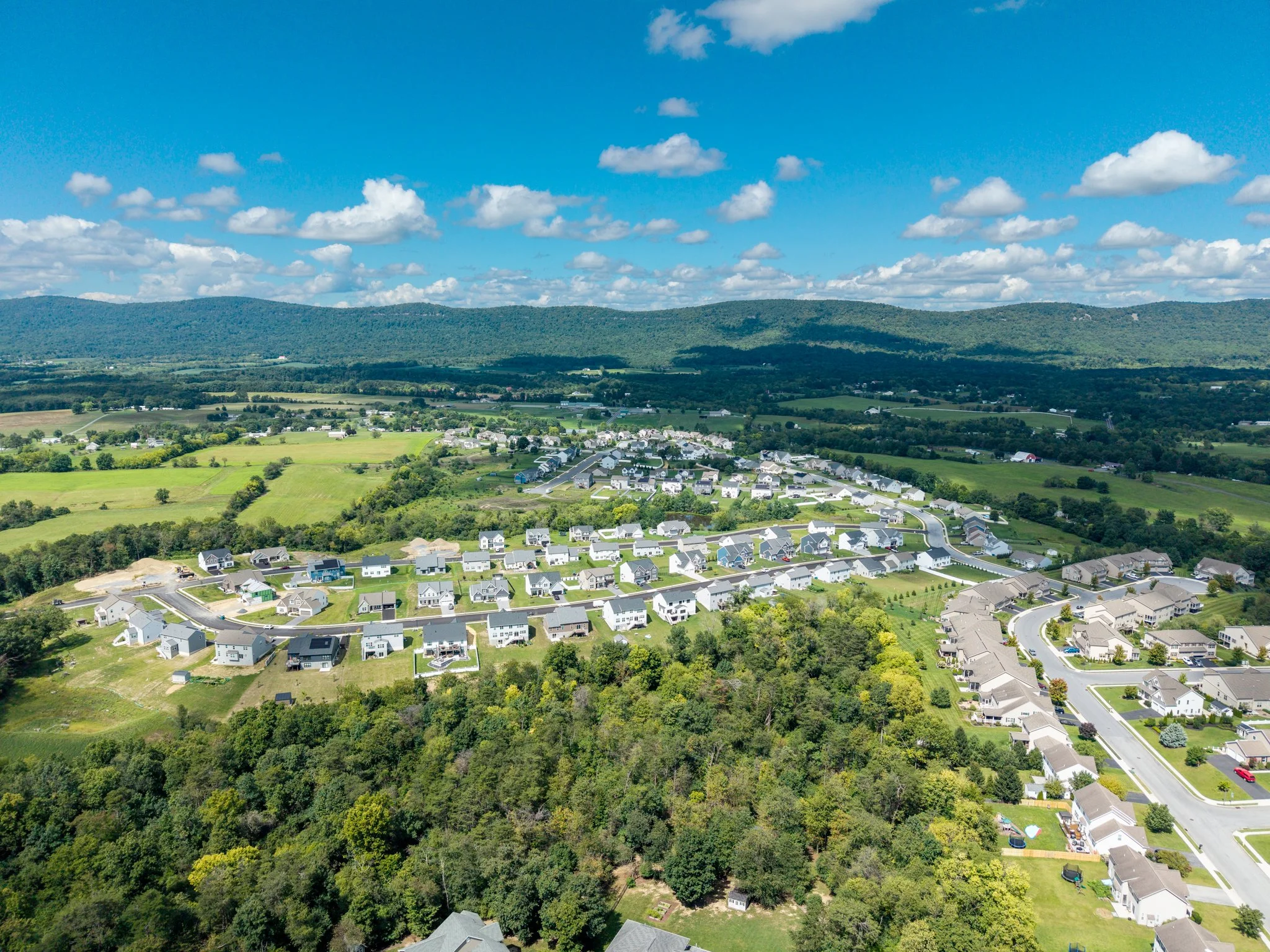 Drone Aerial view of a residential neighborhood at the foot of green, rolling mountains under a partly cloudy blue sky. Carlisle, PA