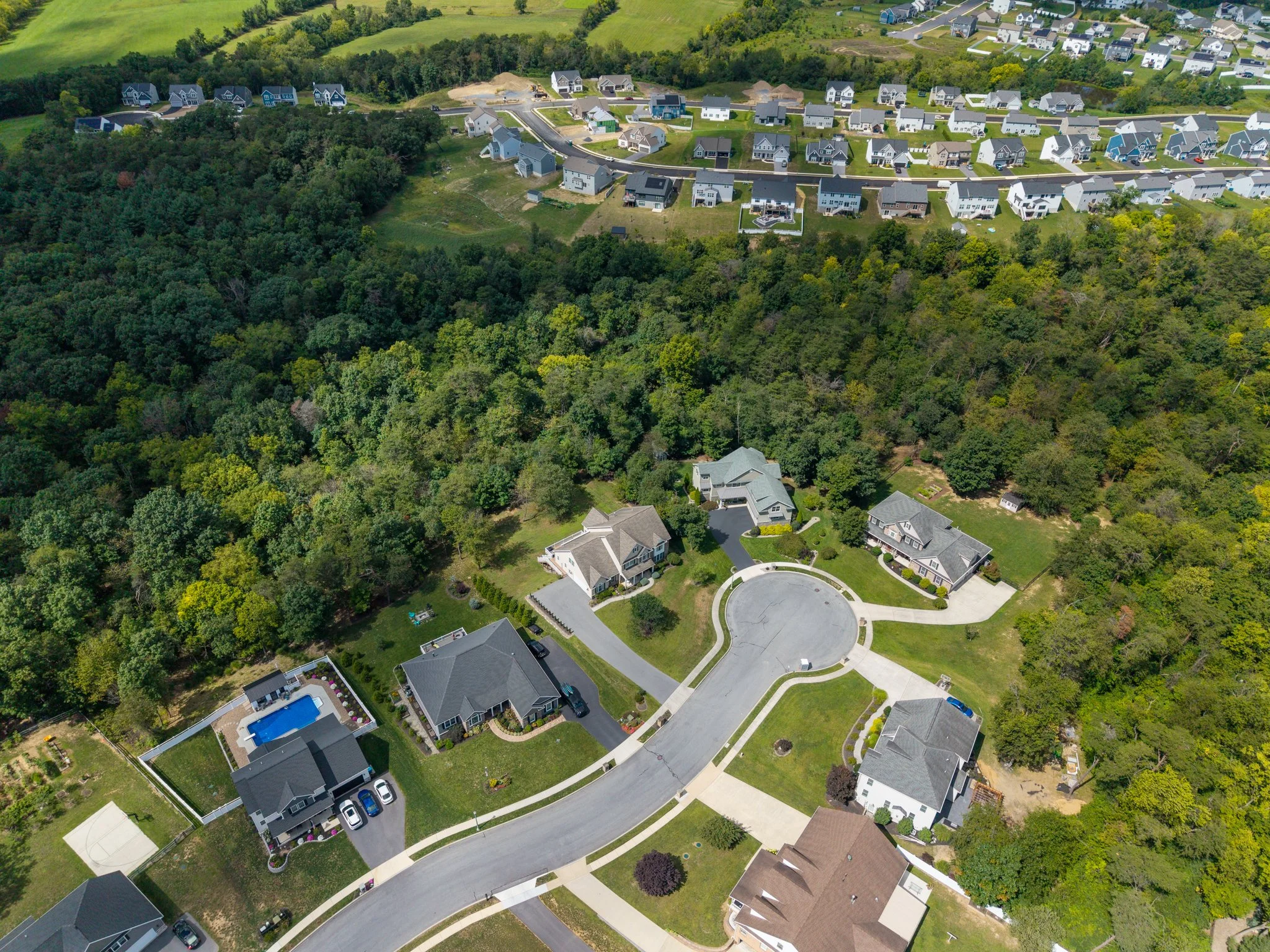 Drone Aerial view of a suburban neighborhood with houses, a curved road, a backyard with a pool, and green trees. Carlisle, PA