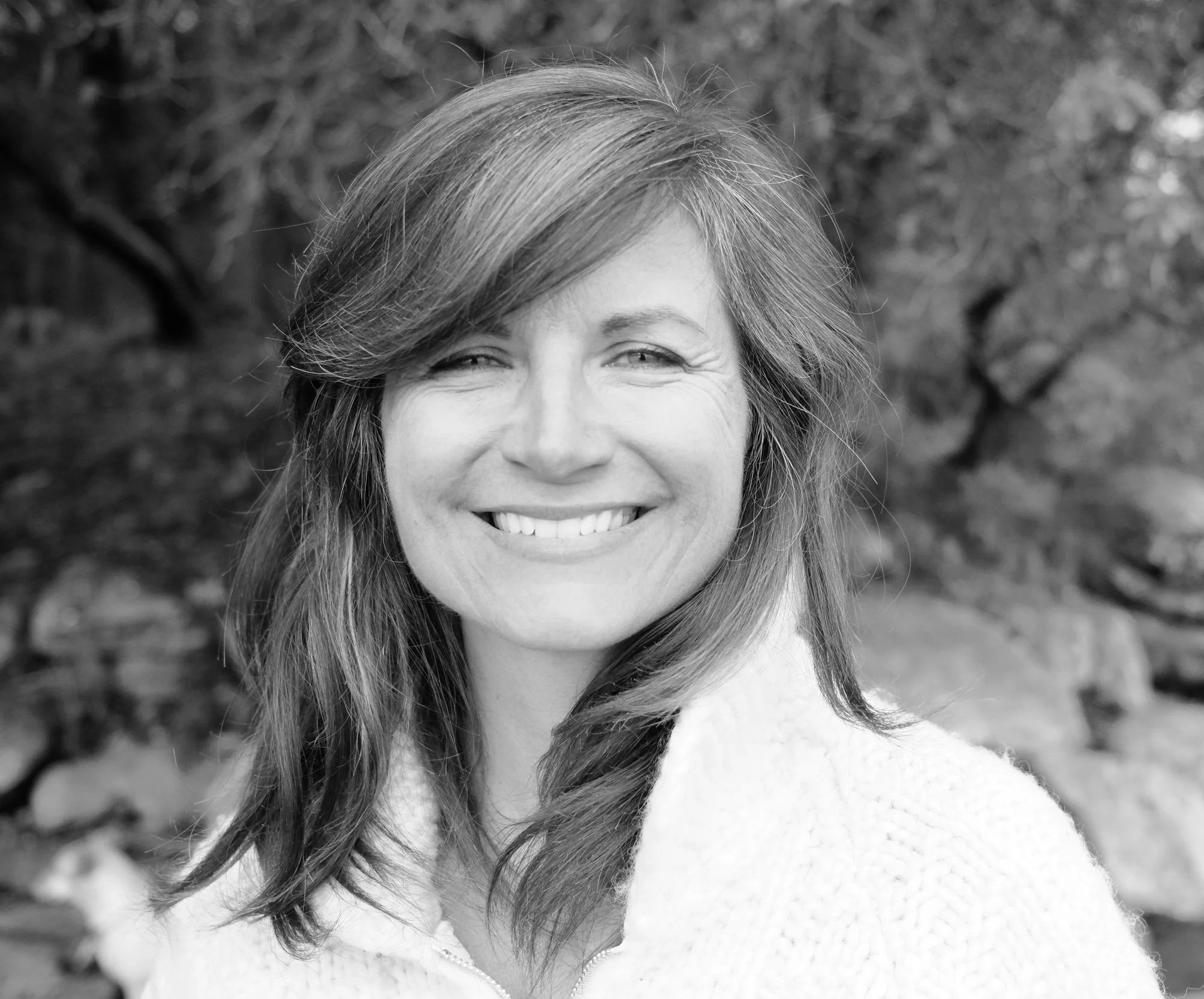 Black-and-white close-up portrait of a smiling woman with long hair, outdoors.