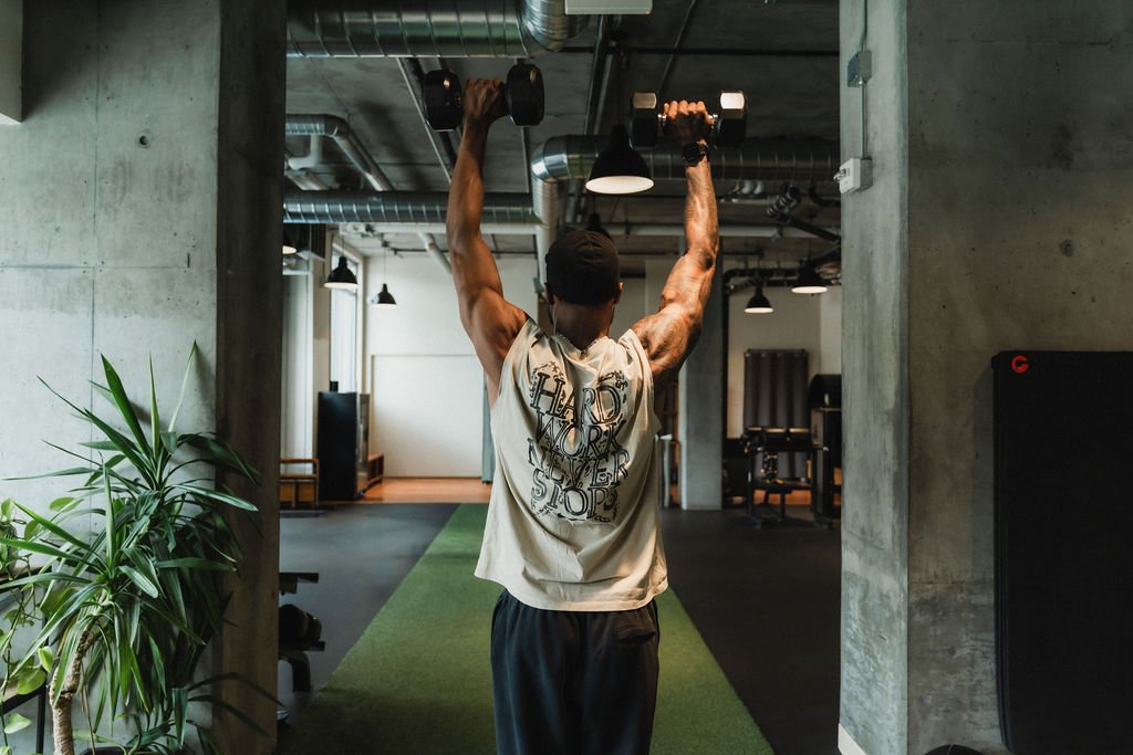 A man lifting dumbbells overhead in a gym.