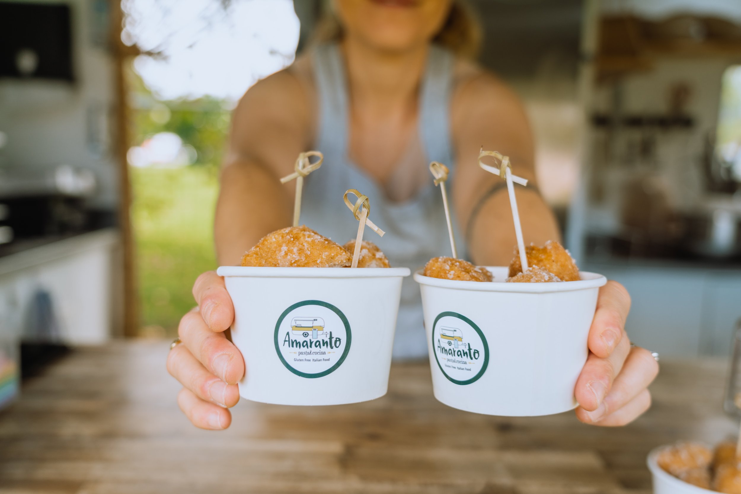 A person holding two cups of breaded, fried food with skewers in a kitchen or outdoor setting.