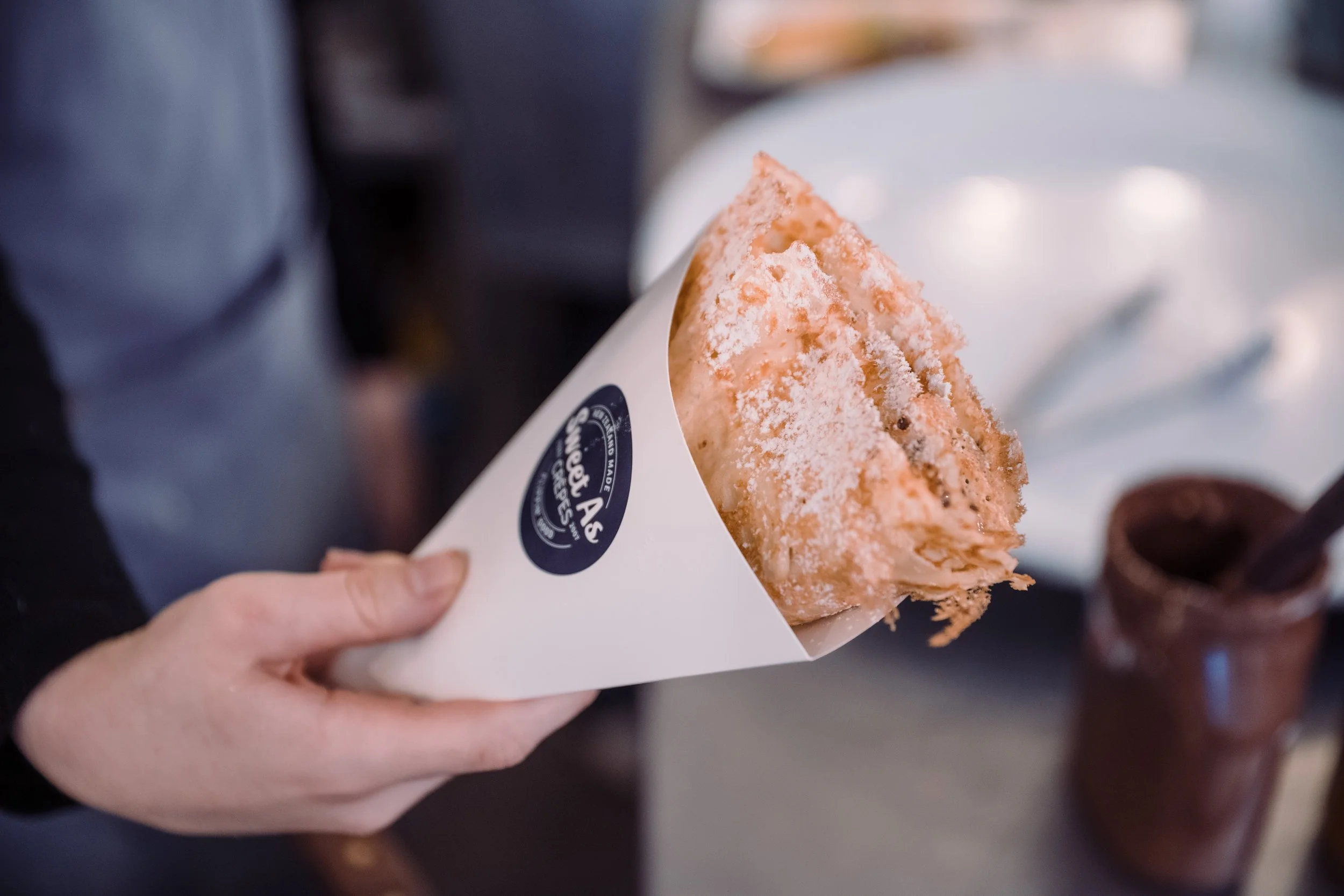 A person holding a triangular piece of toast with powdered sugar on top, in a white paper cone.