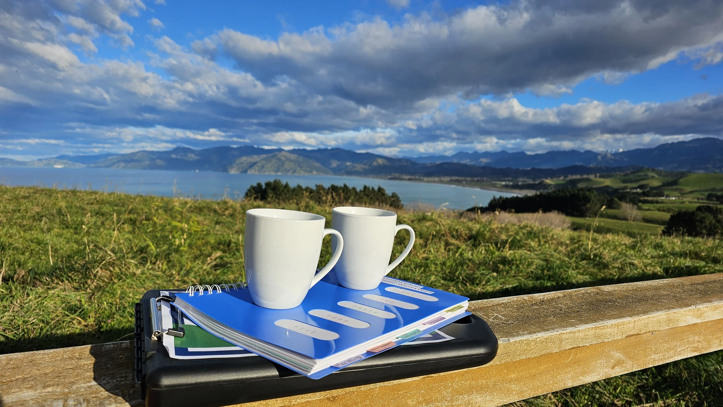 Notebook, coffee mugs and business planning materials overlooking the Nelson landscape, representing practical planning for small business owners.