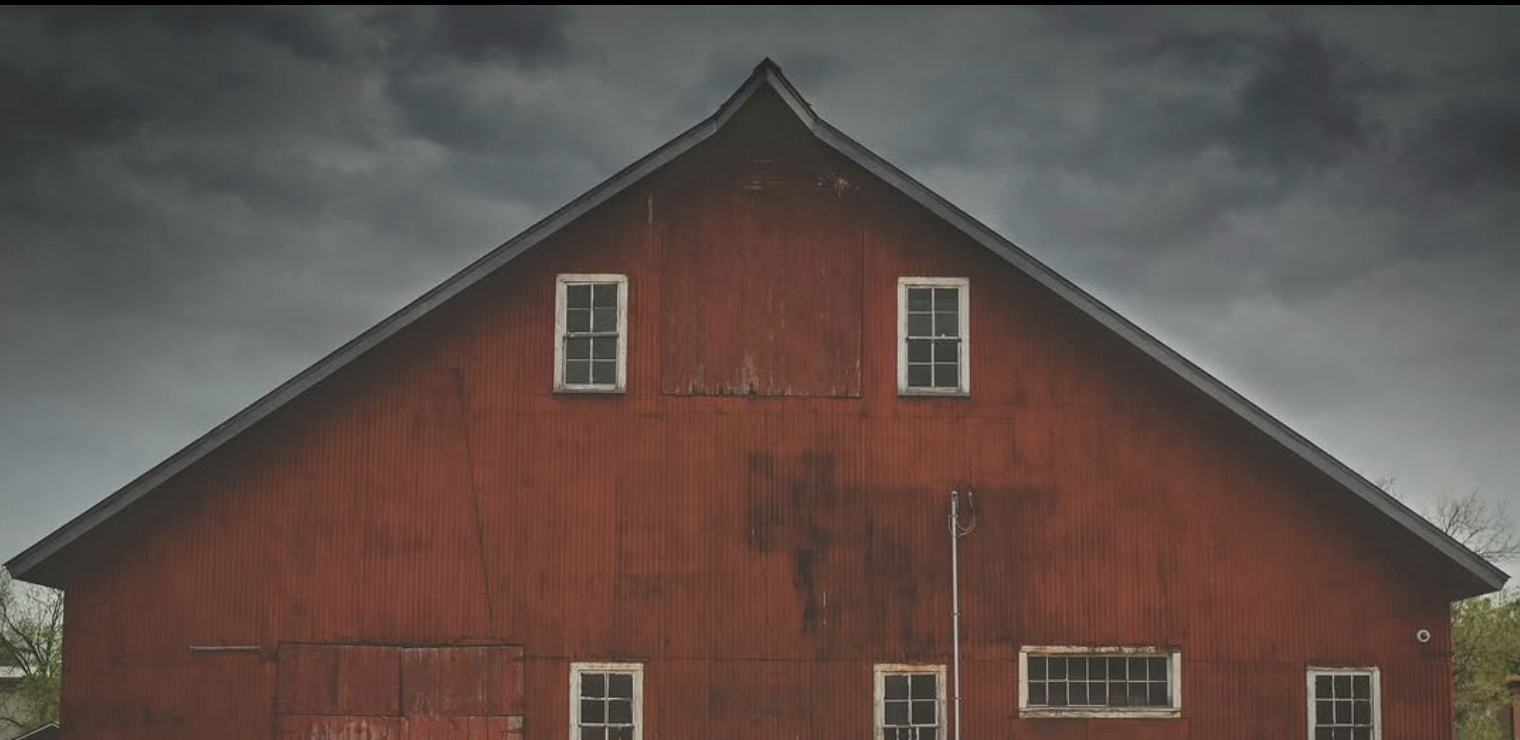 Old, weathered red barn against dark, stormy sky.