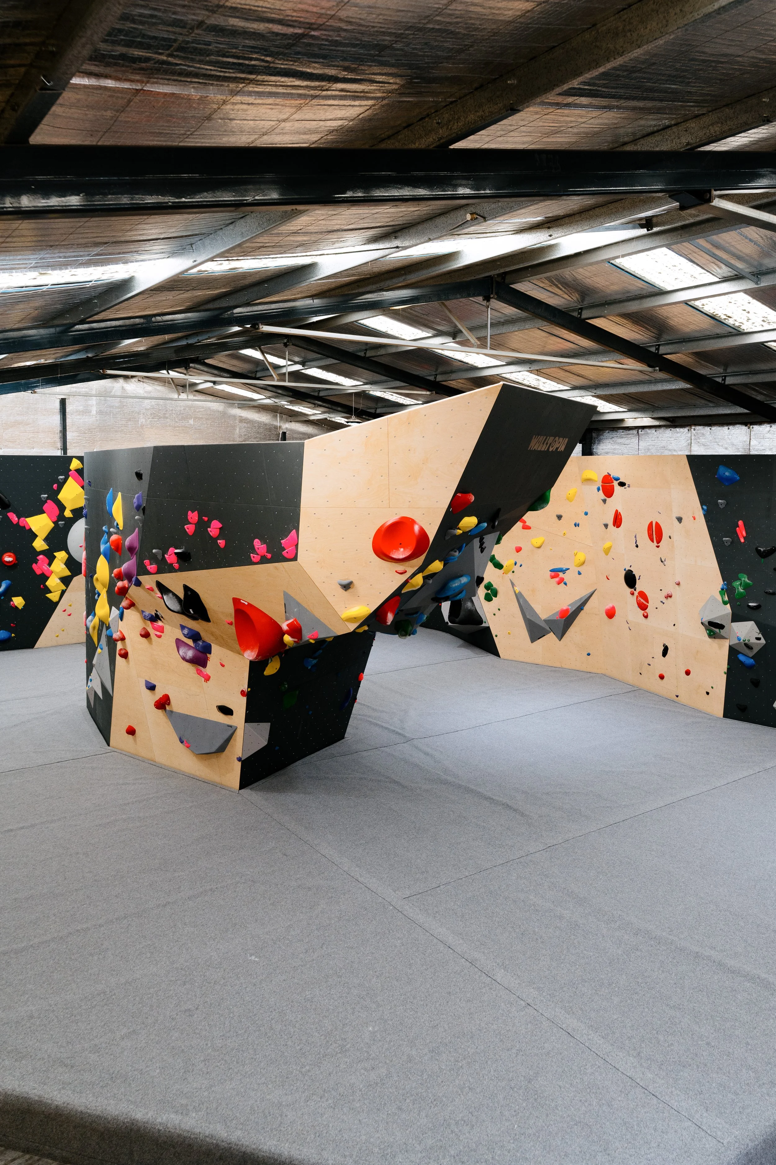 Indoor bouldering gym with climbing holds on a freestanding artificial climbing wall, set on a padded gray floor.