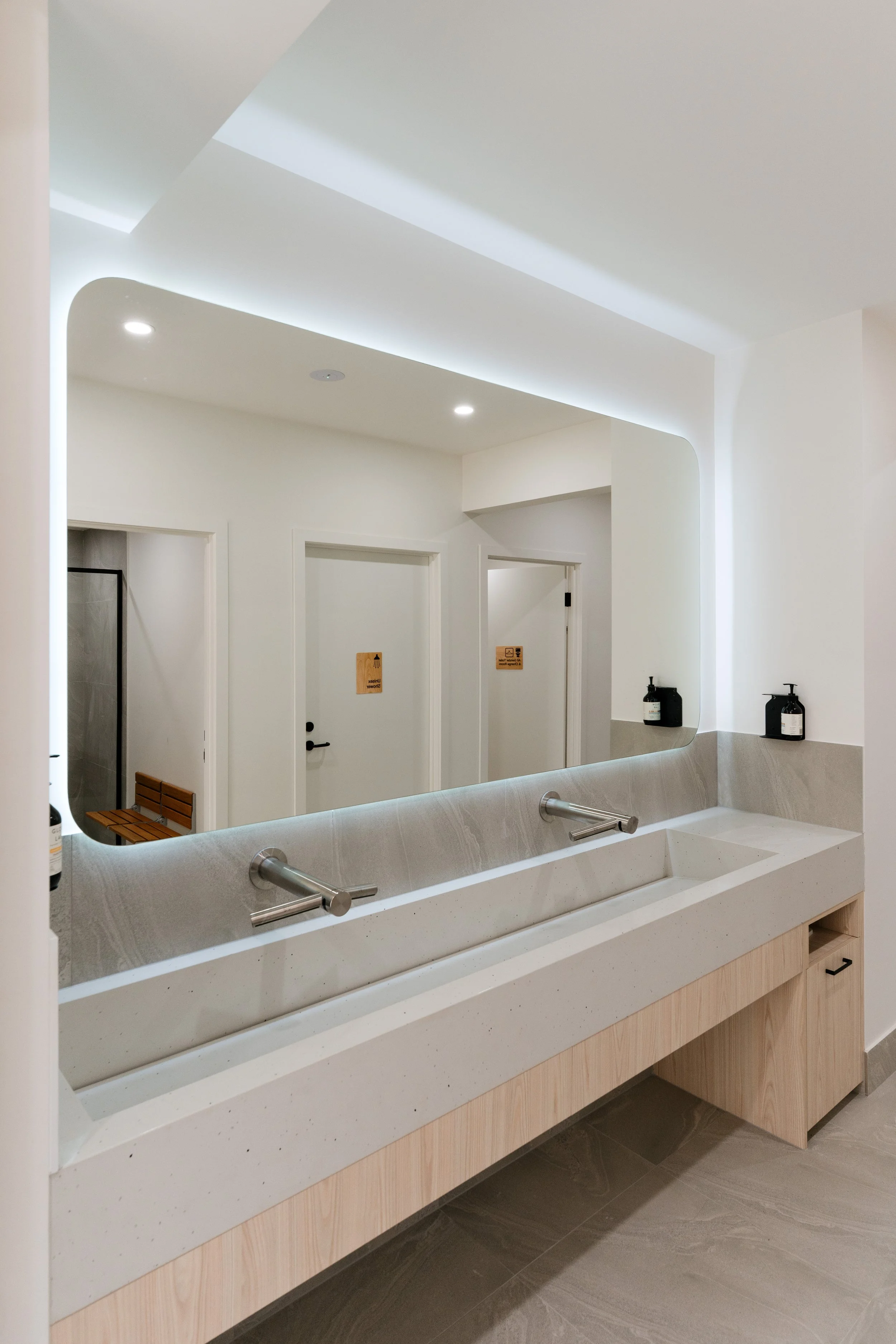 Modern bathroom vanity with a mirror, two soap dispensers, and a double sink with faucets, decoratively illuminated with built-in lighting and clean minimalist design.