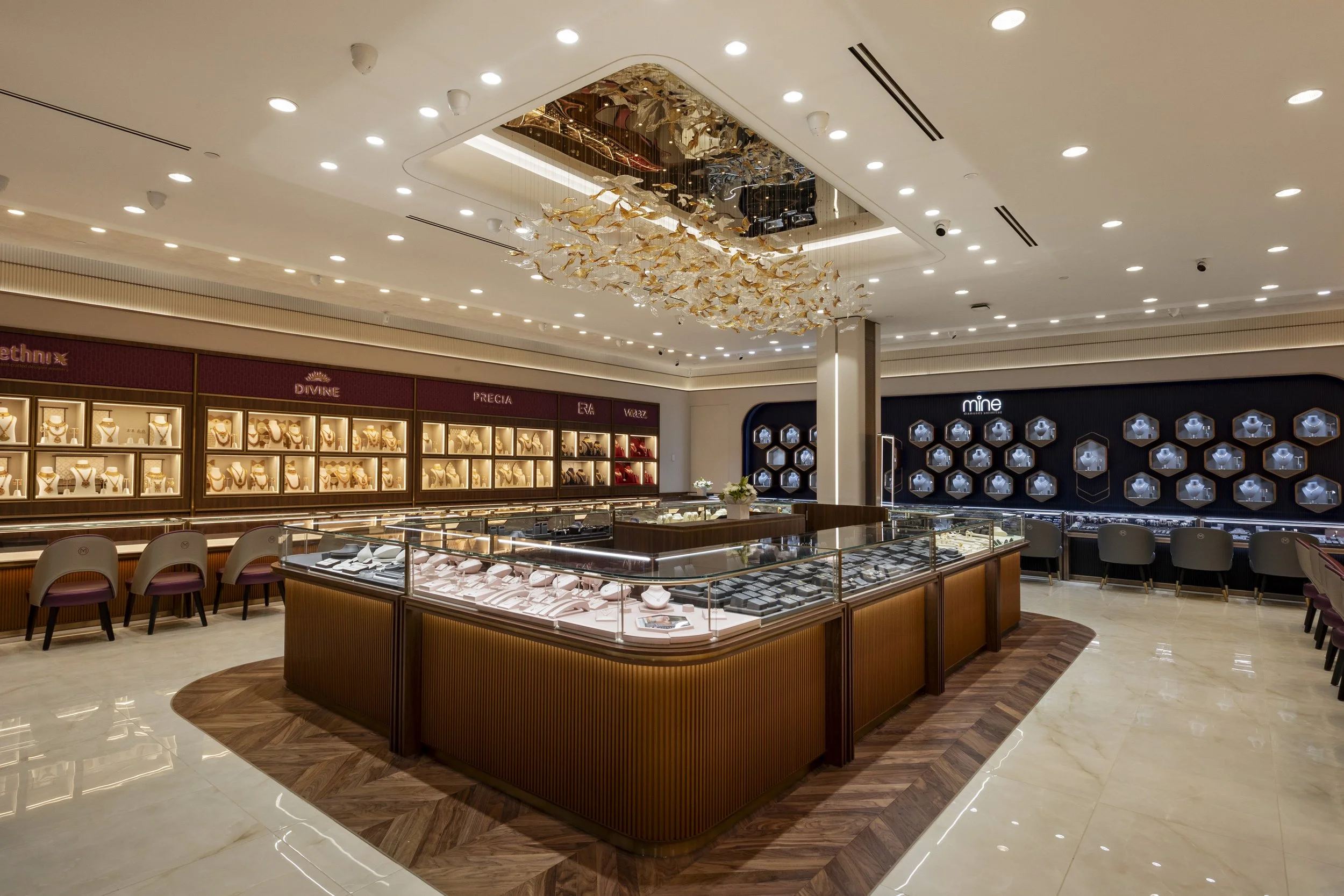 Jewelry store interior with display cases of necklaces, bracelets, and rings, a central wooden display island, and decorative ceiling installation of golden fish, with seating area.