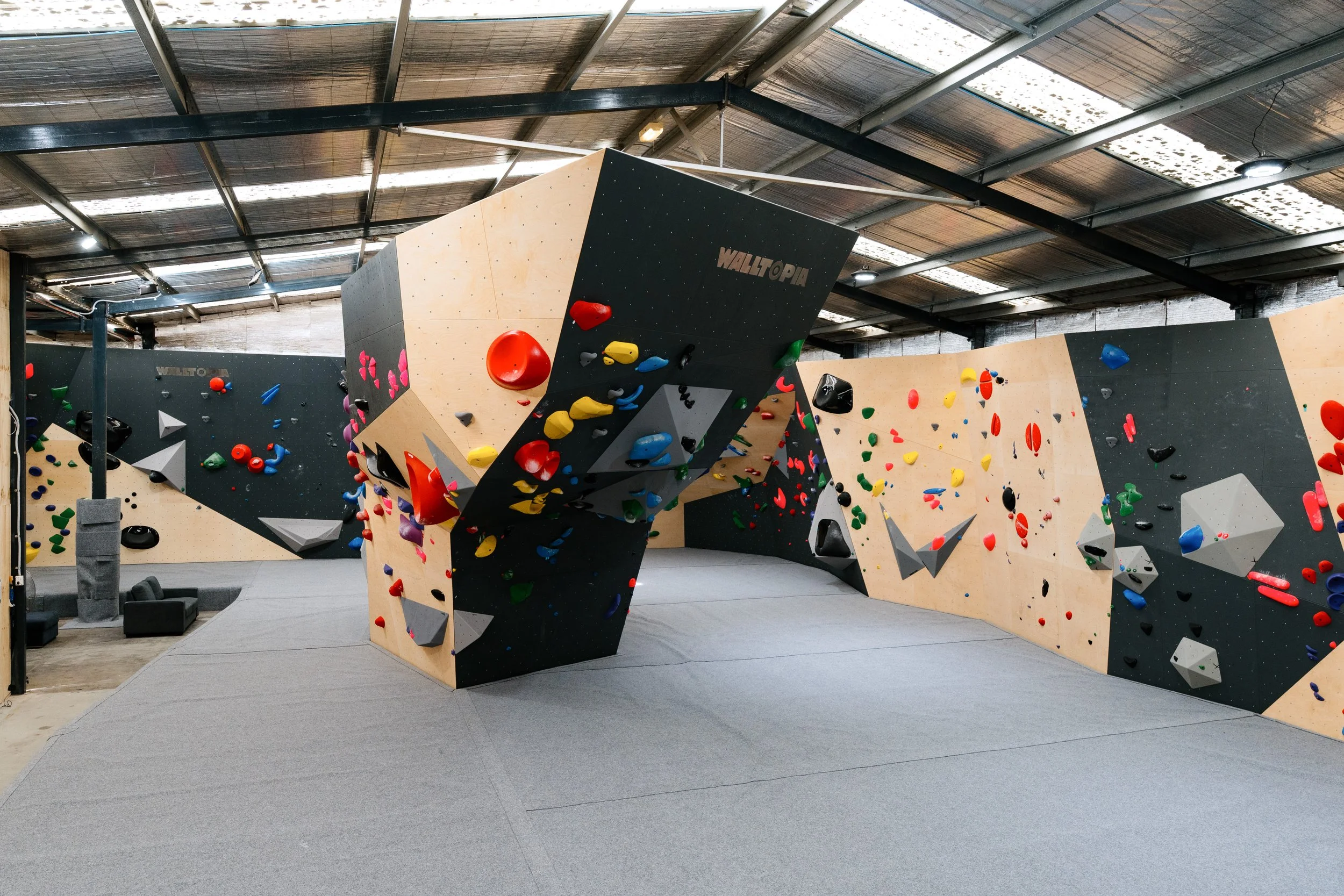 Indoor bouldering gym with various climbing walls covered in colorful holds and padded flooring for safety.