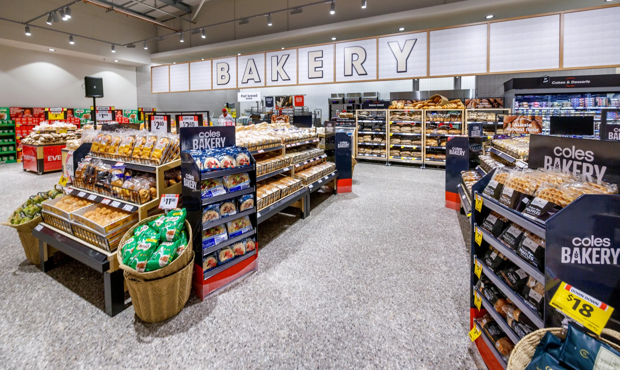 Interior view of a bakery section in a grocery store, displaying shelves with bread, baked goods, and packaged products under a large sign that reads 'BAKERY'.