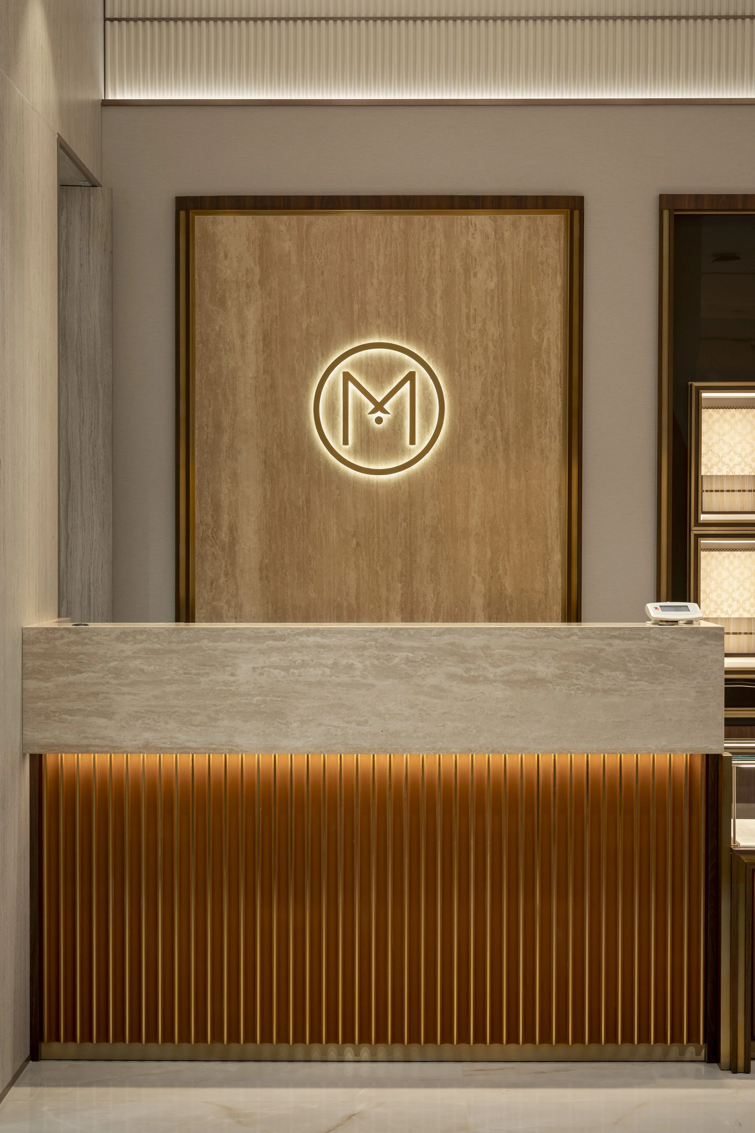 Modern hotel reception desk with a illuminated logo on the wall behind it, made of light wooden paneling and vertical wooden slats below.