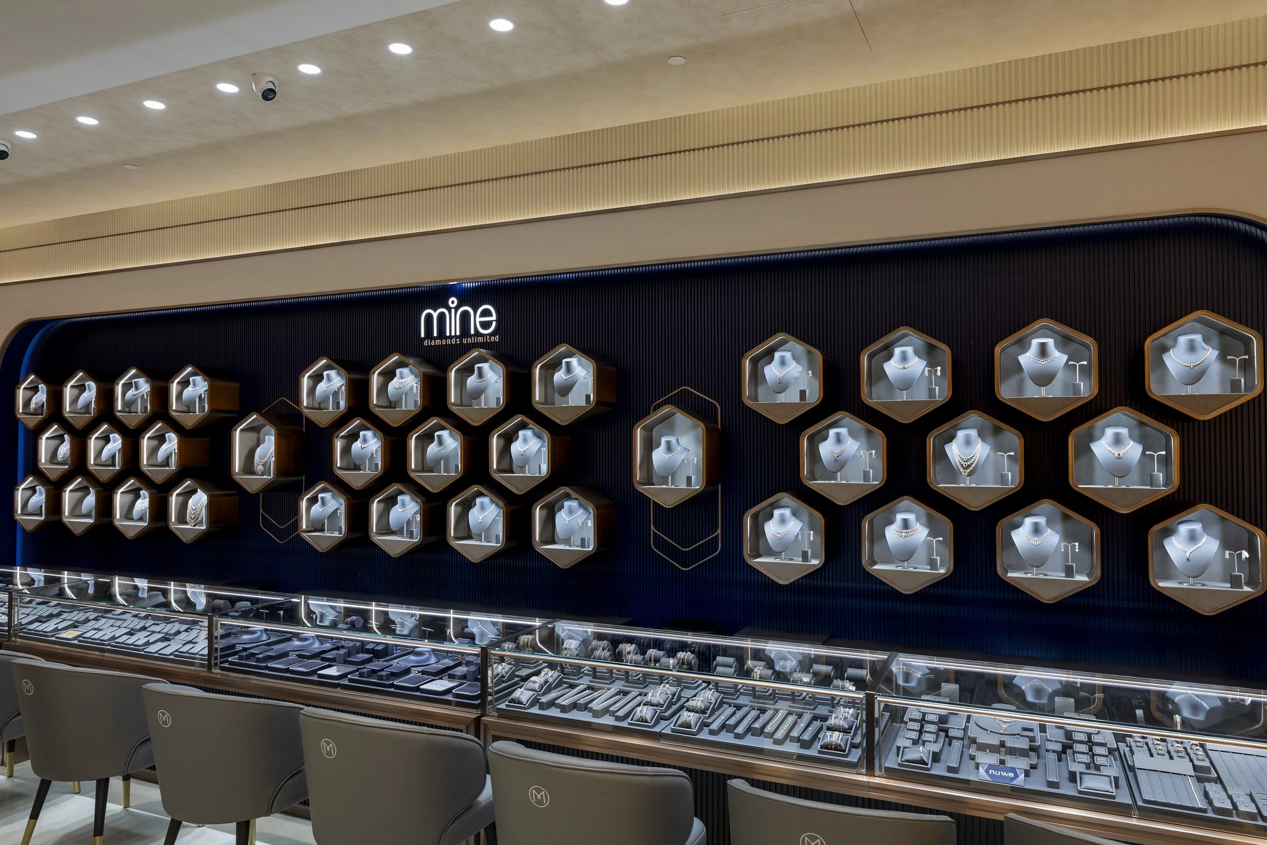 Jewelry display store with various necklaces in hexagonal cases above a glass counter.