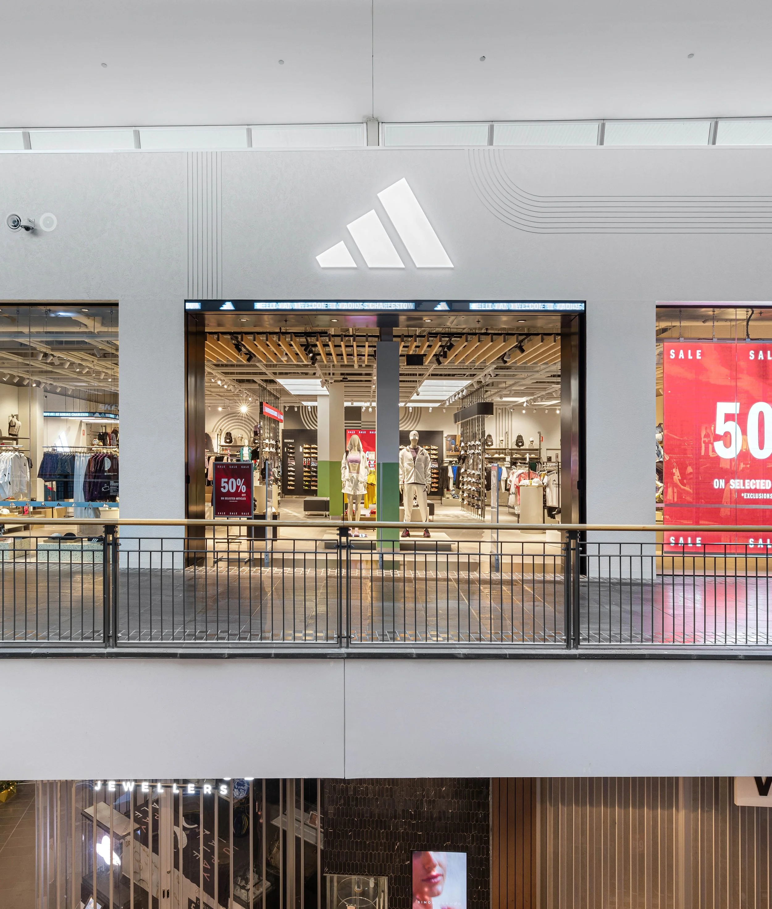 View of a shopping mall interior with a store entrance, mannequins displaying clothing, and sale signs advertising 50% off.
