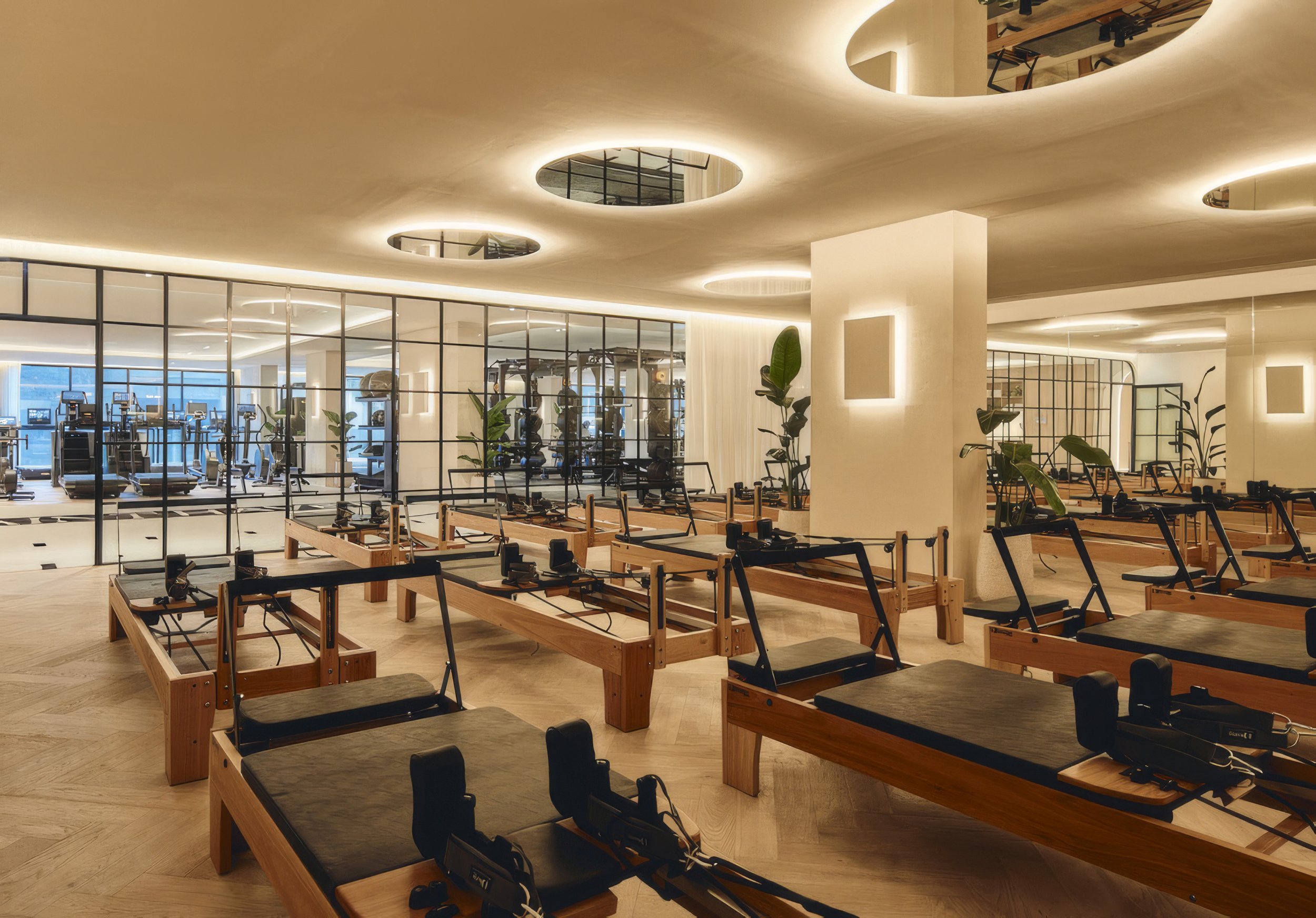 Empty fitness room with Lohr Pilates beds, black chairs, and plants, featuring a ceiling with round cutouts and warm lighting.
