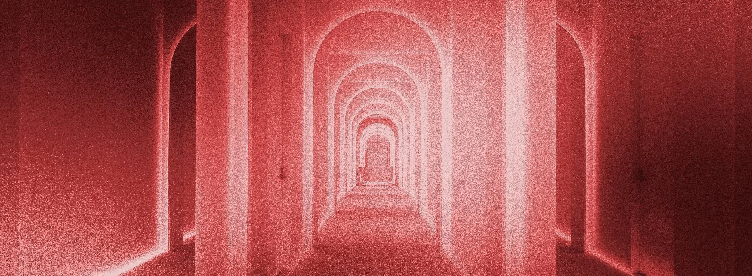 A long corridor with multiple arches, painted in shades of pink and red creating a tunnel like effect.