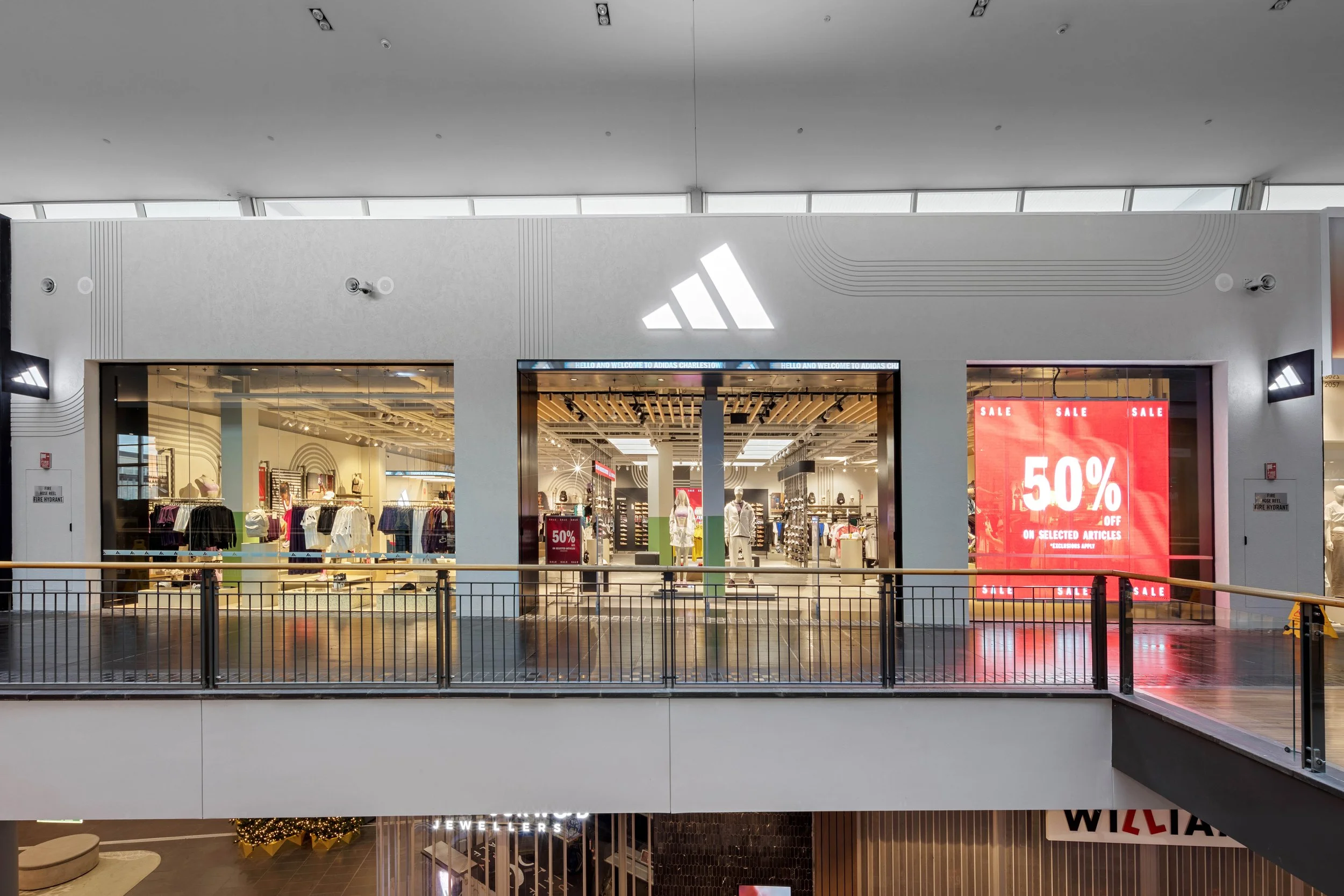 Exterior view of a retail store in a mall, with a large digital sale sign showing 50% off, and mannequins dressed in clothing inside the store.