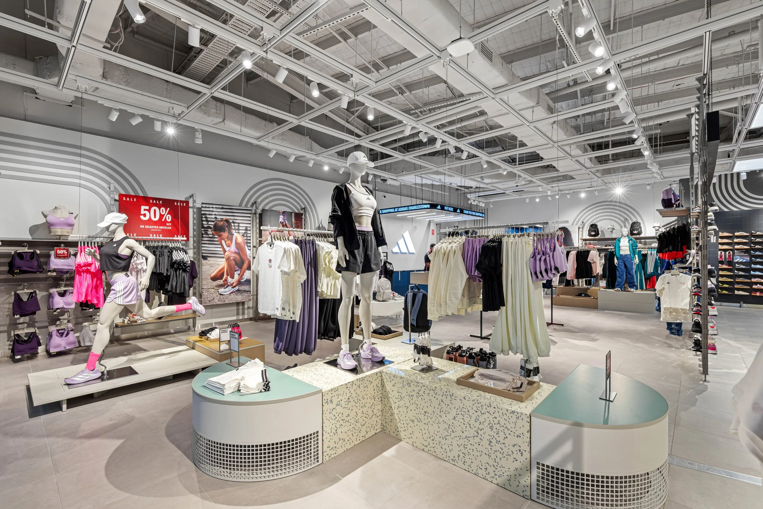 Interior of a clothing store with mannequins displaying athletic wear, shelves with folded clothes, sale signs, and overhead lighting.