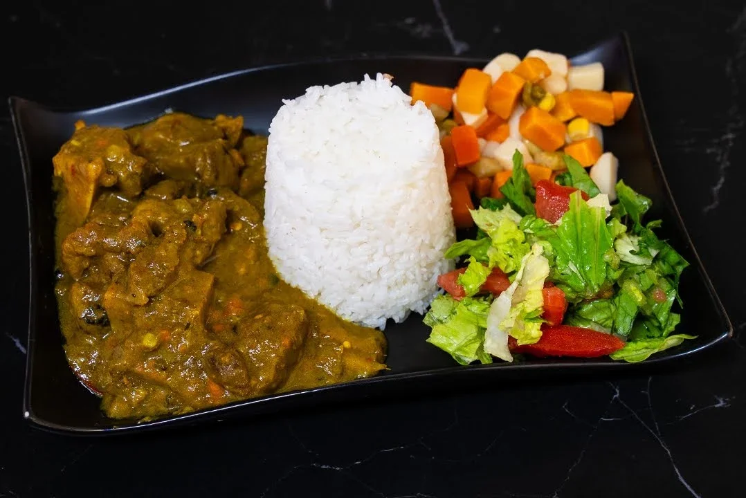 Plate of steaming white rice, beef curry with sauce, chopped carrots, cauliflower, and green leafy salad with tomatoes.