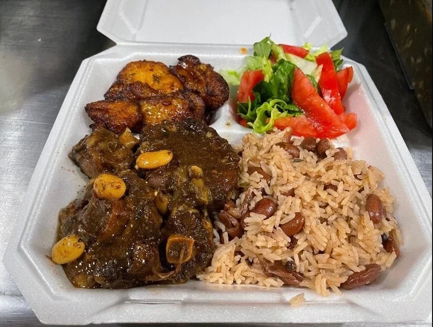 Takeout meal with rice, beans, steak, plantains, and salad in a foam container.