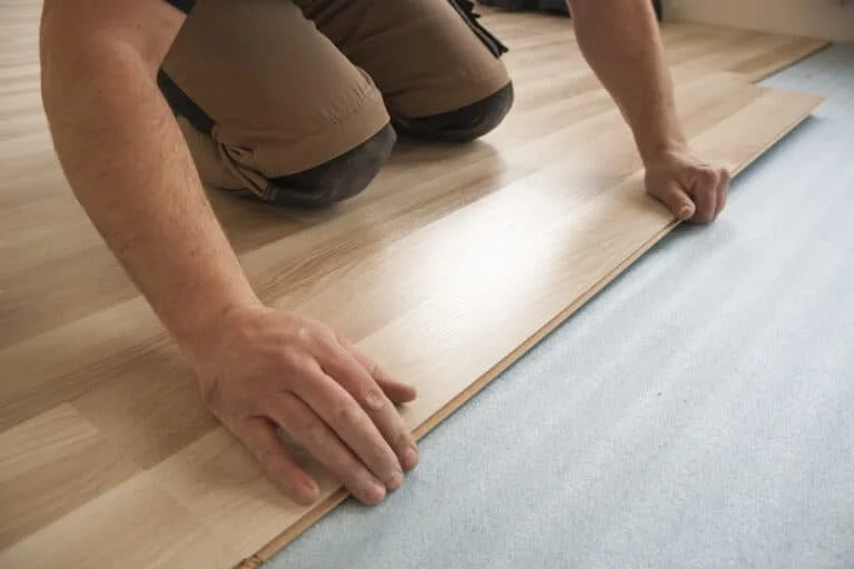 Person installing laminate flooring, kneeling on the floor, aligning a wood plank.
